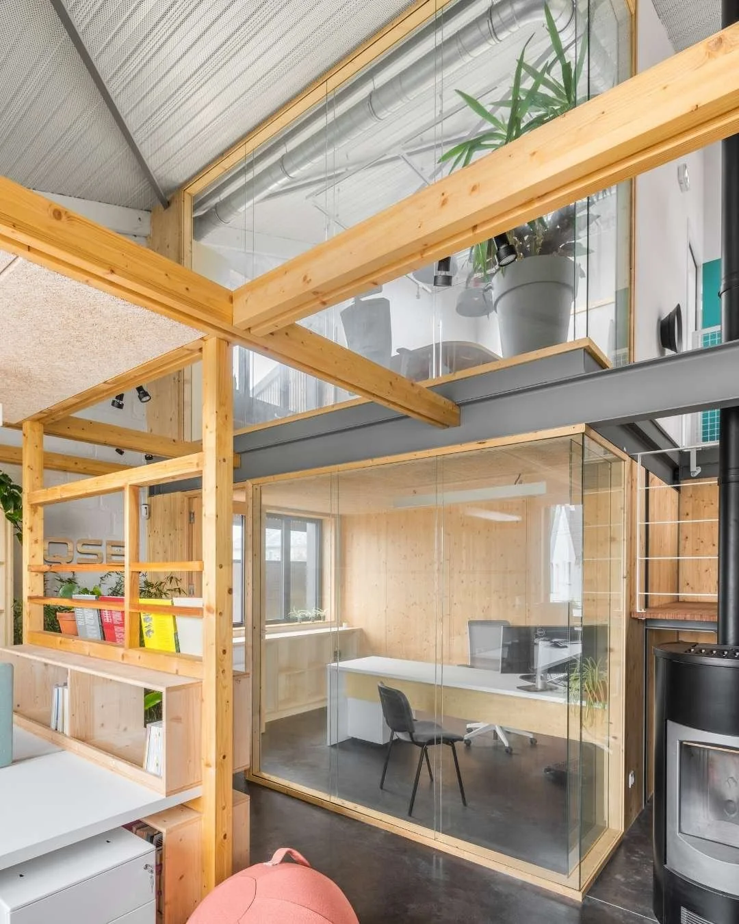 Bureau  de direction vitrée sous une mezzanine avec structure bois apparente et poële à bois comme à la maison.