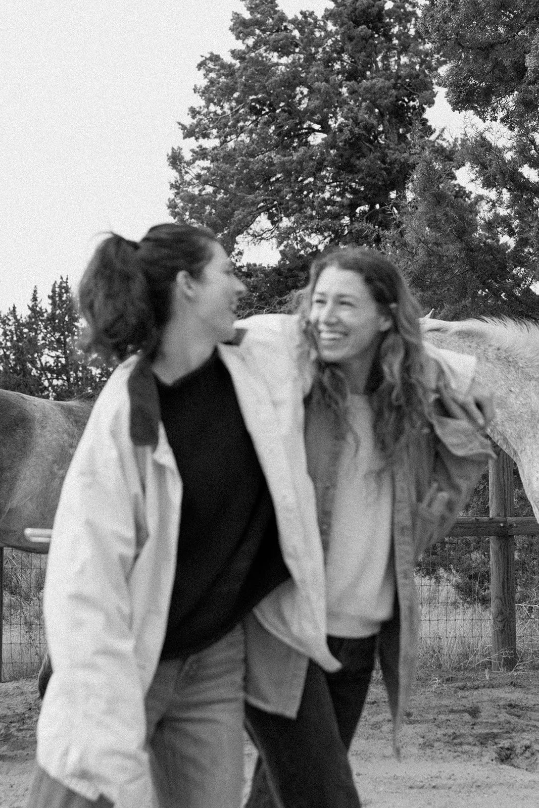 Robin and Kylen smiling and walking together outdoors, with horses and trees in the background.