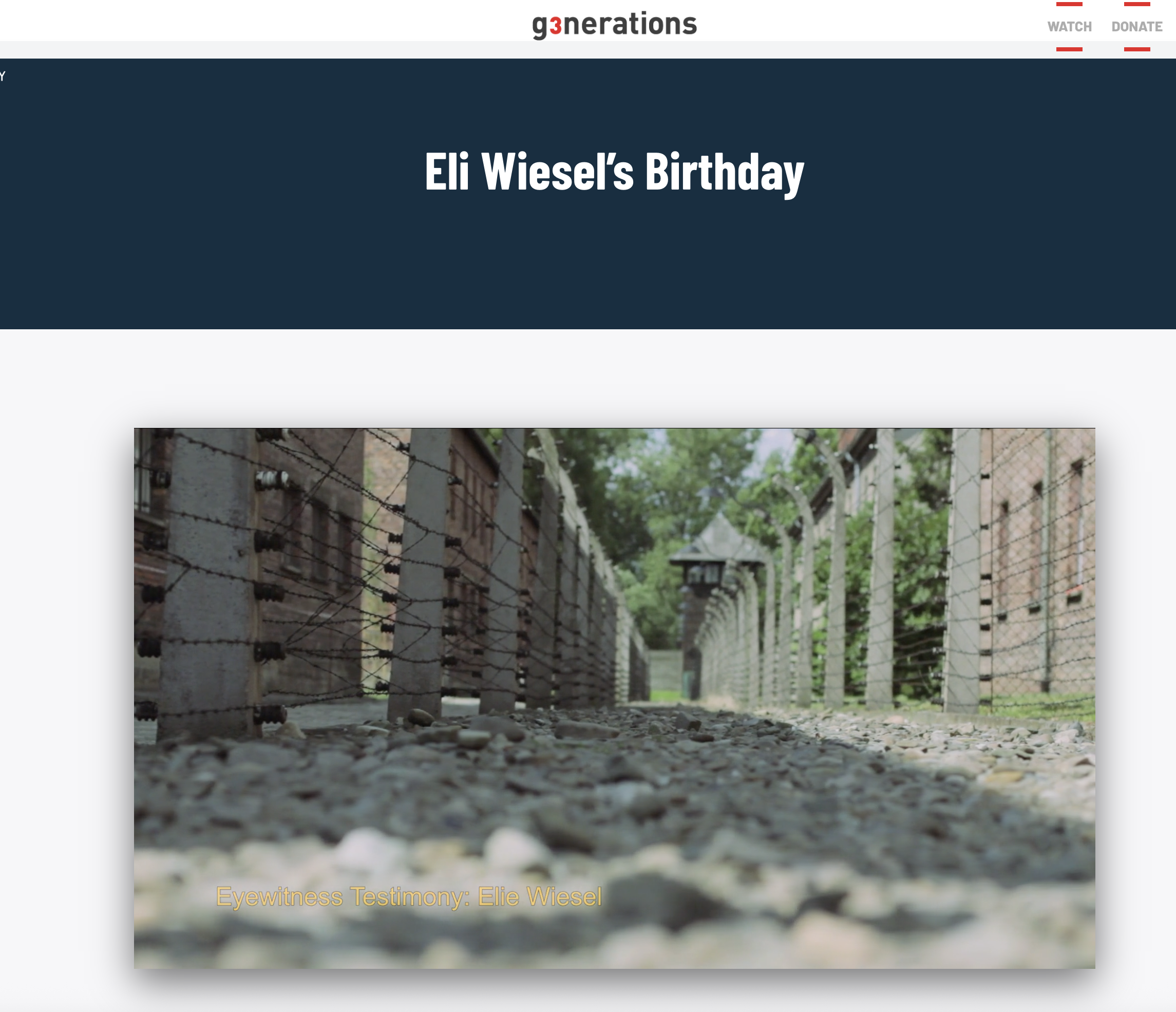 Close-up of the ground with gravel and stones, with a view of a barbed wire fence and a brick building in the background, part of a memorial site.