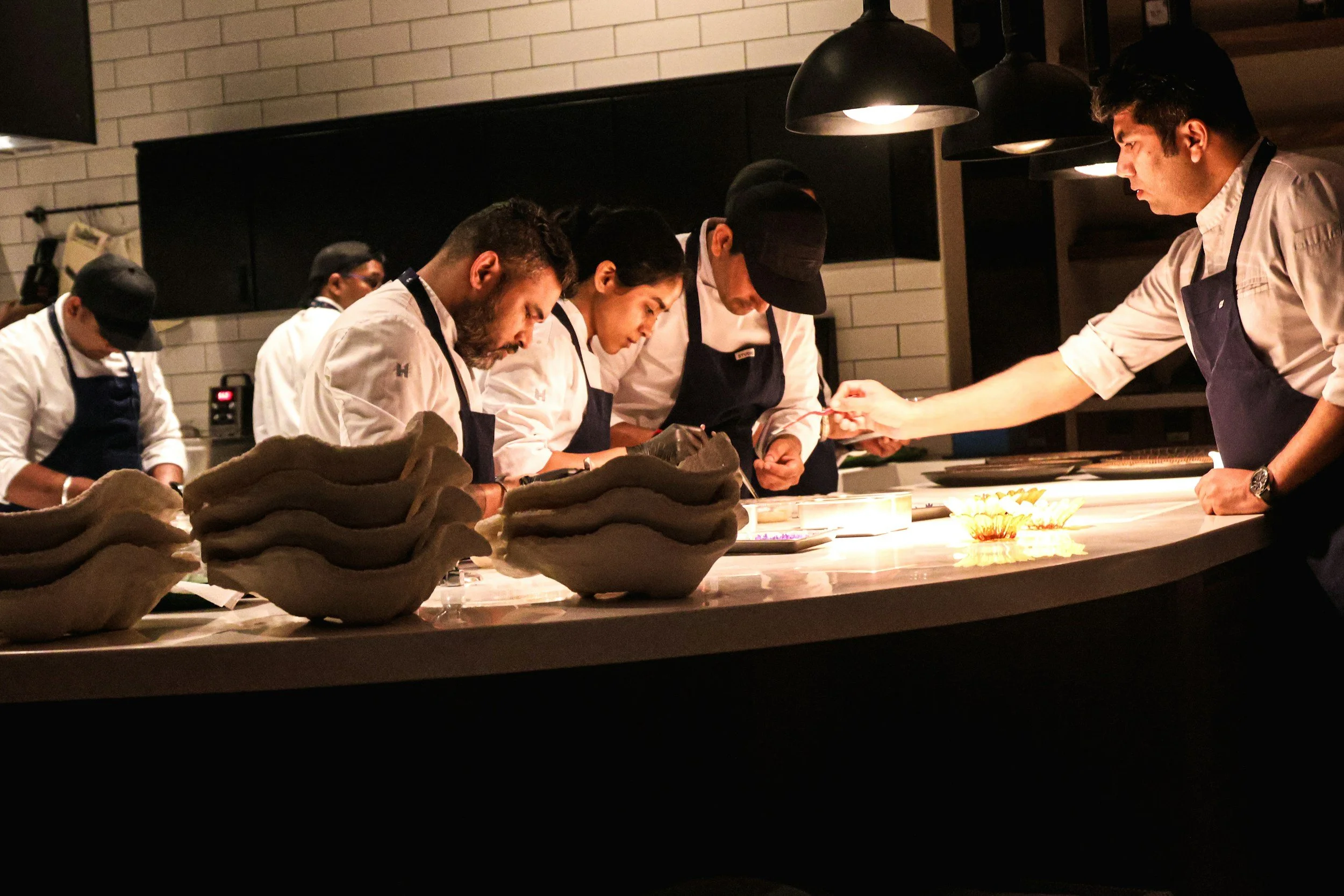 Group of professional chefs and cooks working together in a modern restaurant kitchen, preparing food at a shared counter.