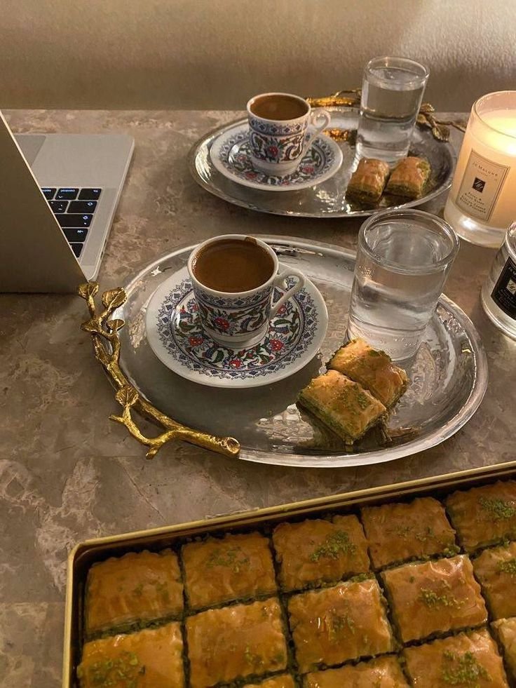 Two cups of Turkish tea on ornate saucers, with glasses of water and baklava on silver trays, in a turkish cafe that is traditional and symbolizes local food and drink scene