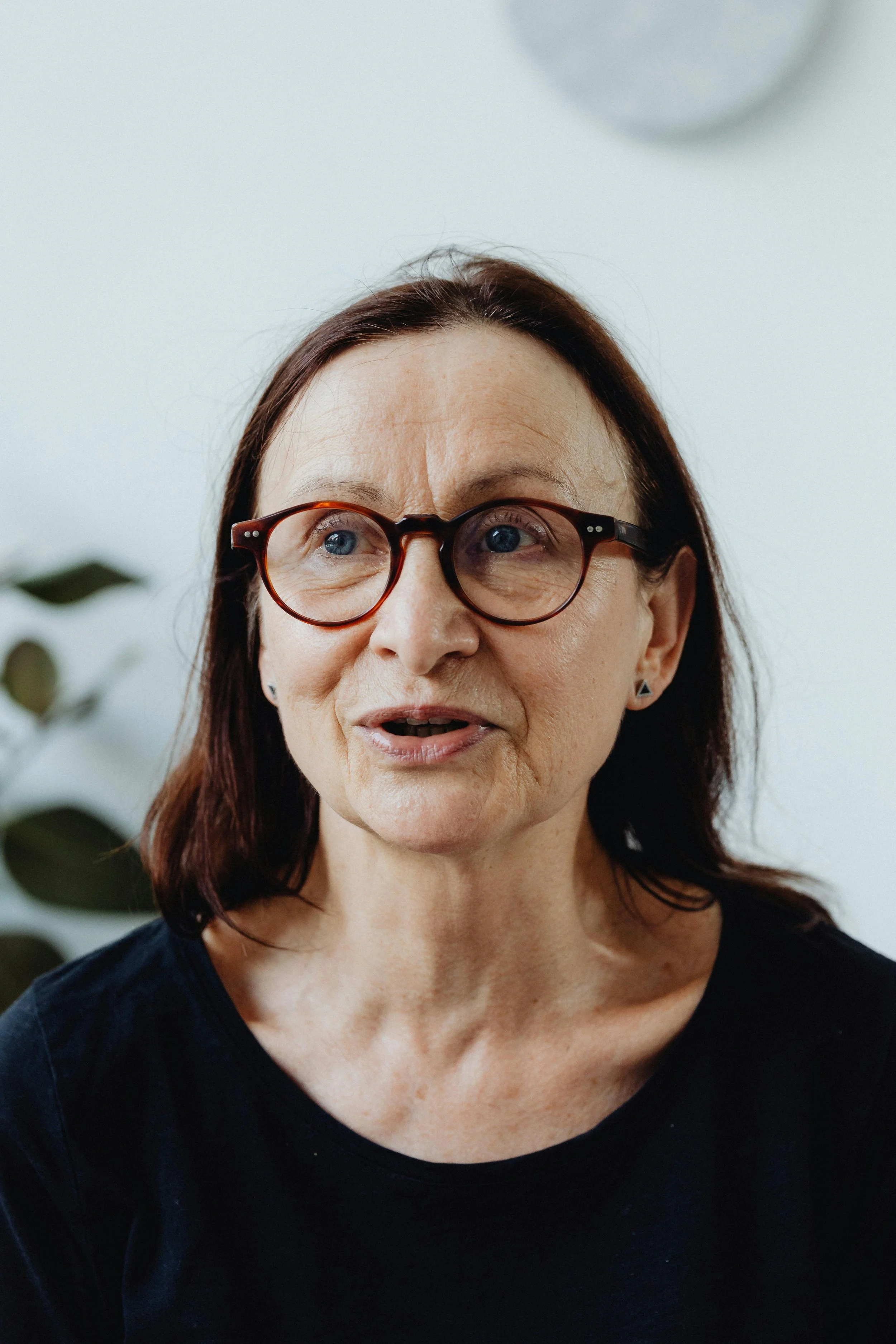 A middle-aged woman with brown hair, wearing glasses, speaking in an indoor setting.