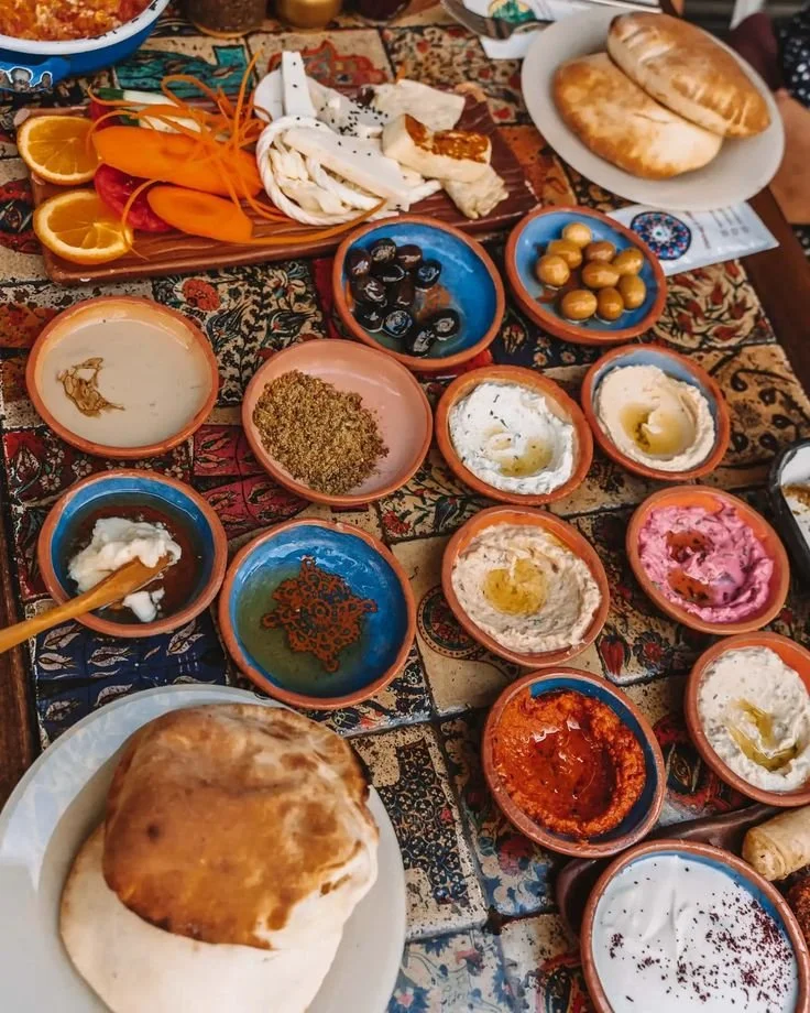 An assortment of Turkish Meze on a table, including various dips, breads, olives, and sliced vegetables such as oranges, strawberries, and carrots showing the culinary vibrancy of turkish food