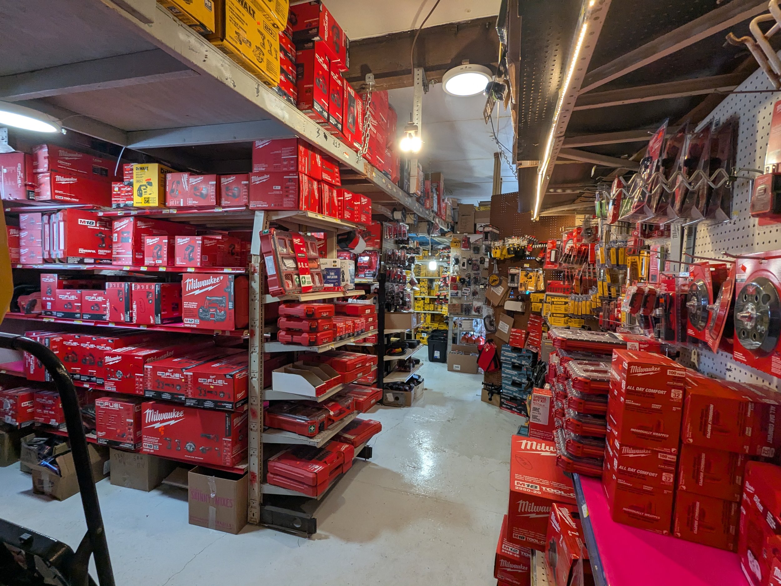A hardware store aisle filled with Milwaukee power tool boxes, accessories, and tools on metal and pegboard shelves.