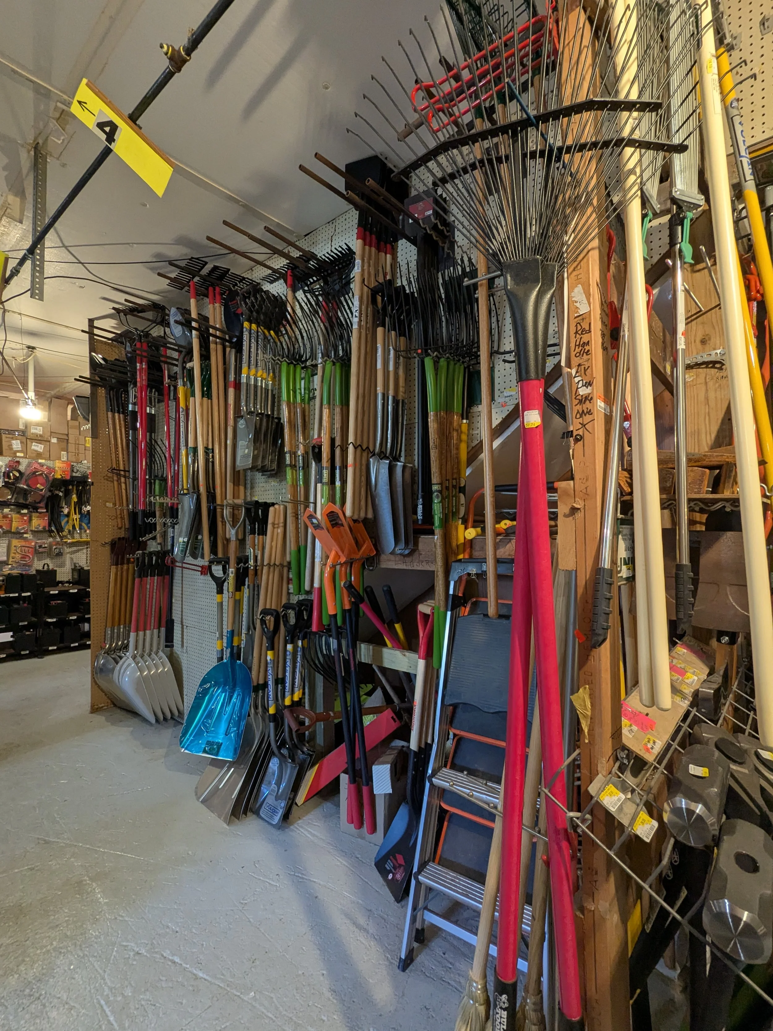 Various gardening tools including rakes, shovels, hoes, and ladders hanging on a display in a hardware store.