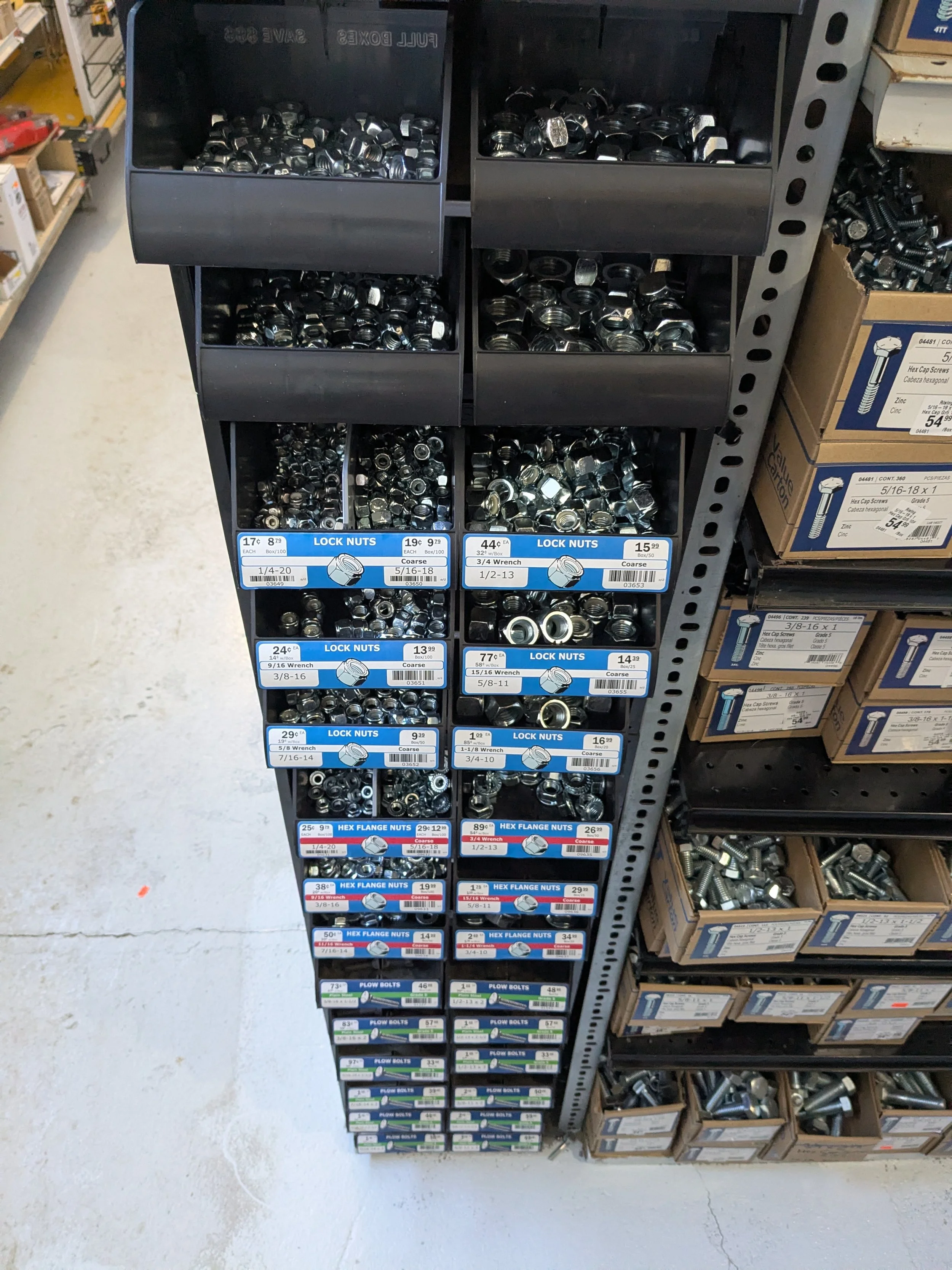 A hardware store display shelf with various types of nuts, including lock nuts and hex flange nuts, organized in small containers and bins.