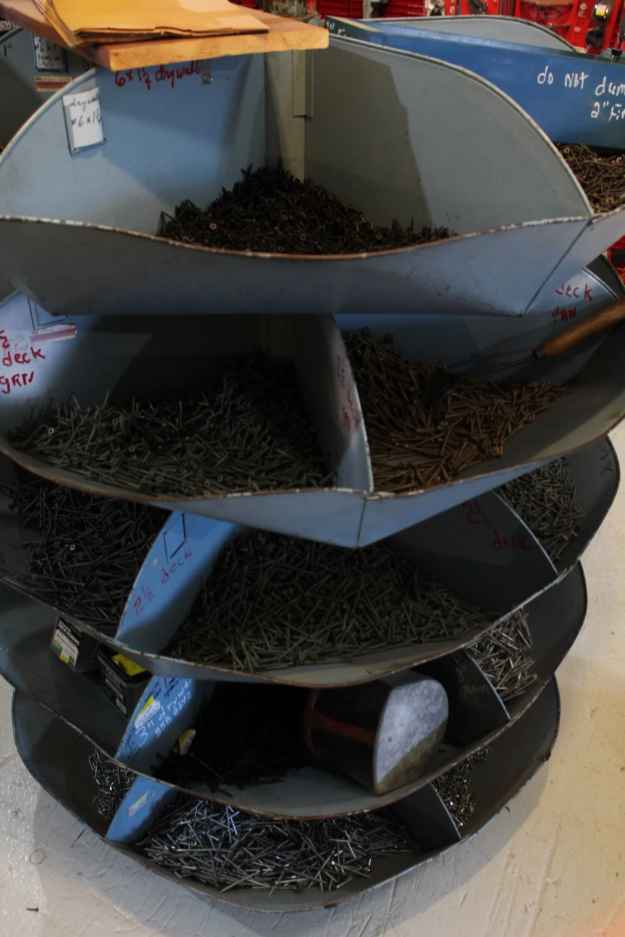 Metal storage shelves filled with various types of nails separated by size and type, with handwritten labels indicating the sizes.