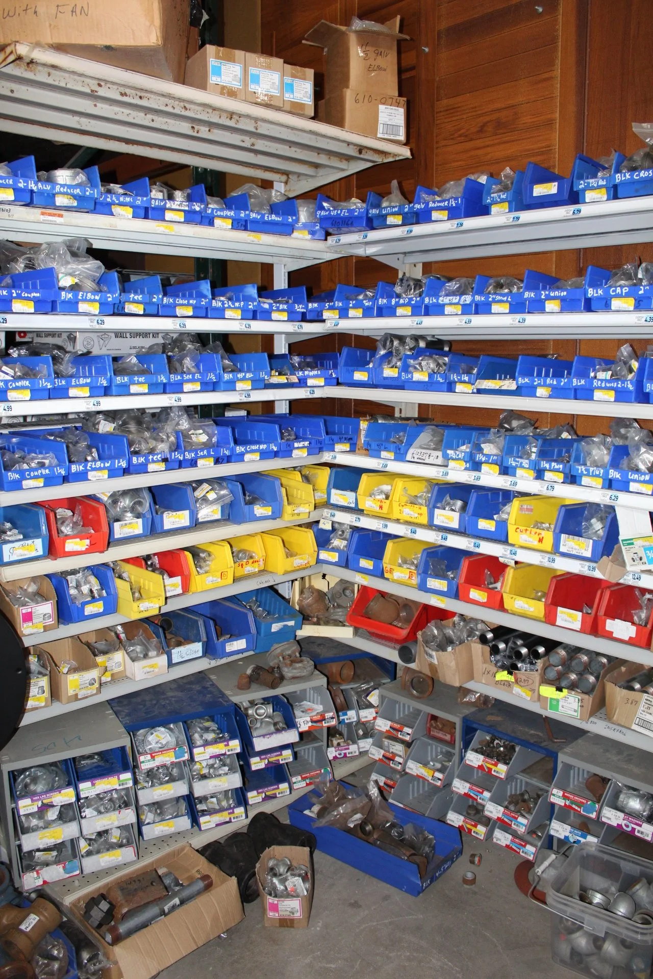 Shelves filled with various plumbing fittings and hardware parts in a hardware store or storage room.