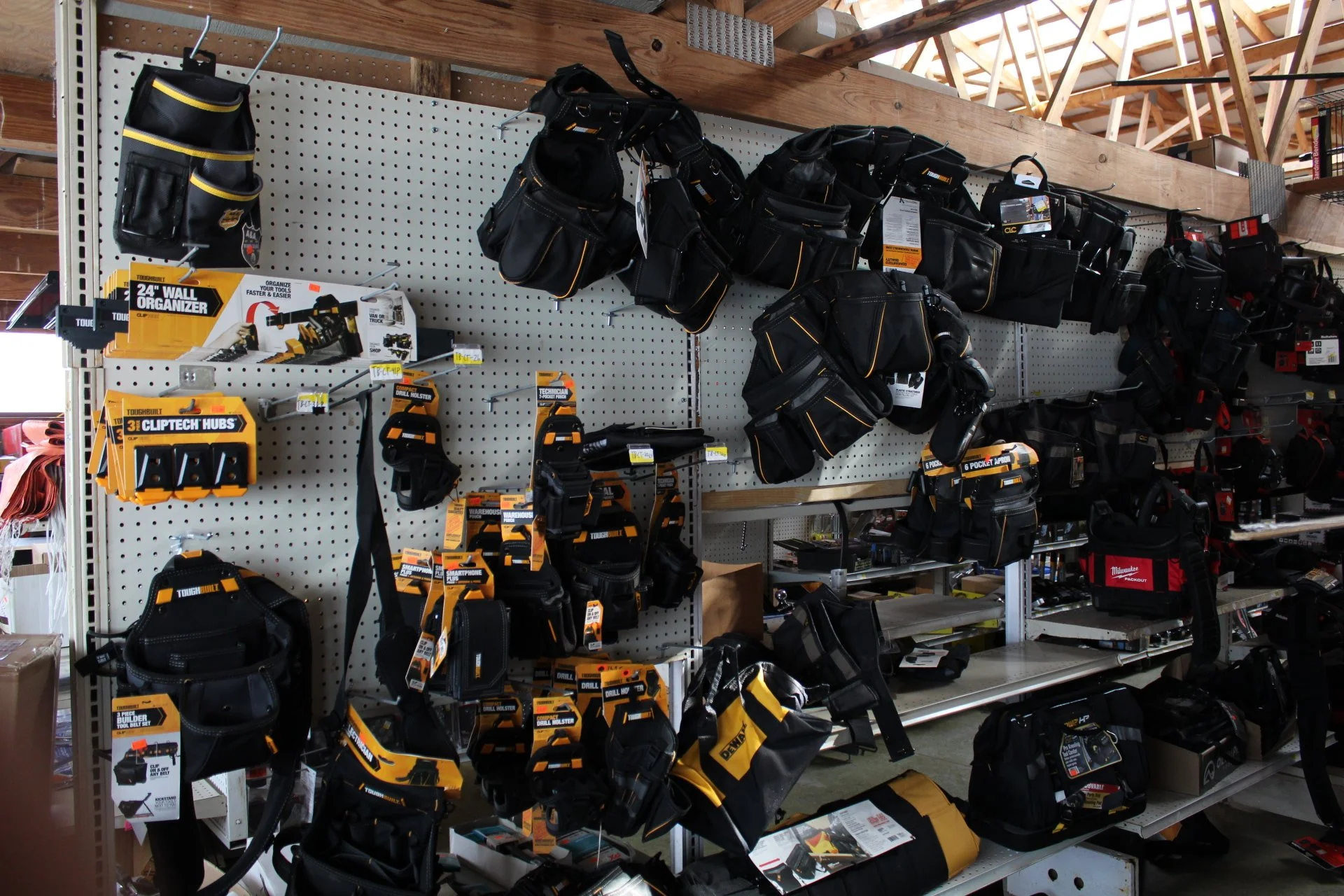 Display of power tool tool belts and gear hanging on a retail store pegboard wall.