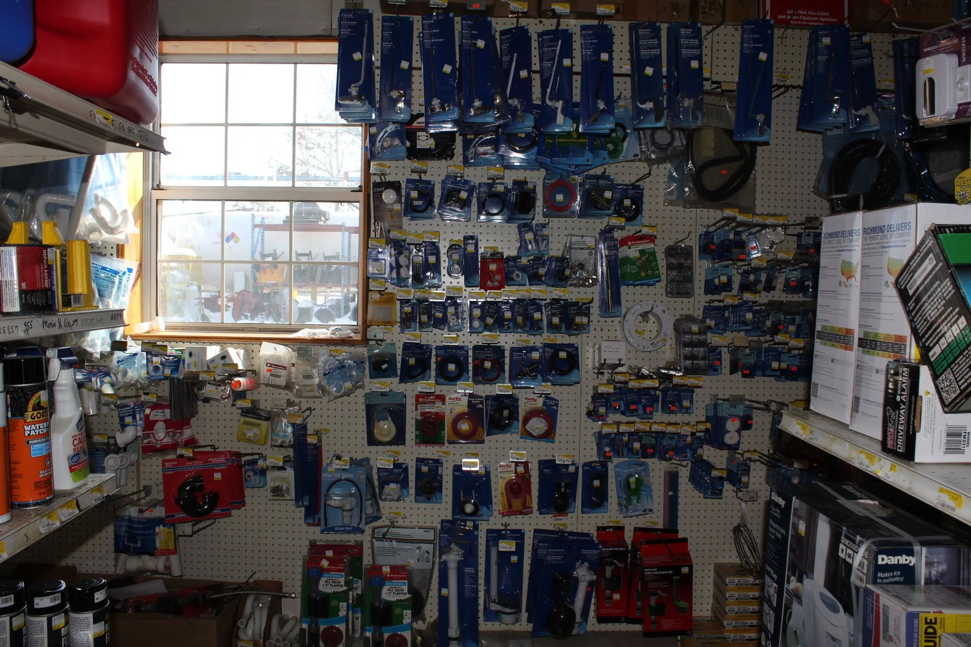 A hardware store shelf with various plumbing and hardware tools and supplies, illuminated by natural light from a window.