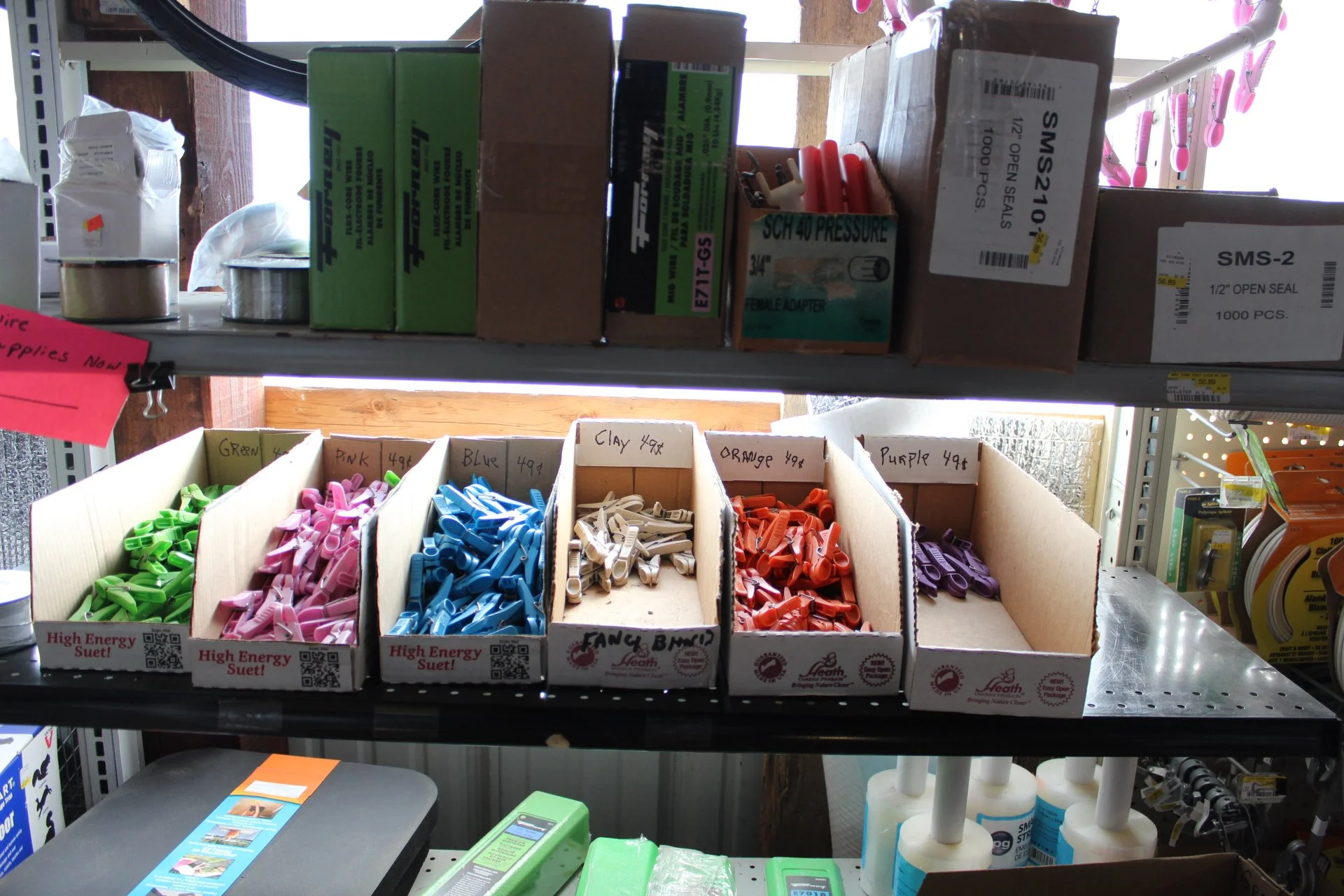 Colored zip ties sorted by color in small cardboard boxes on a metal shelf in a hardware store.