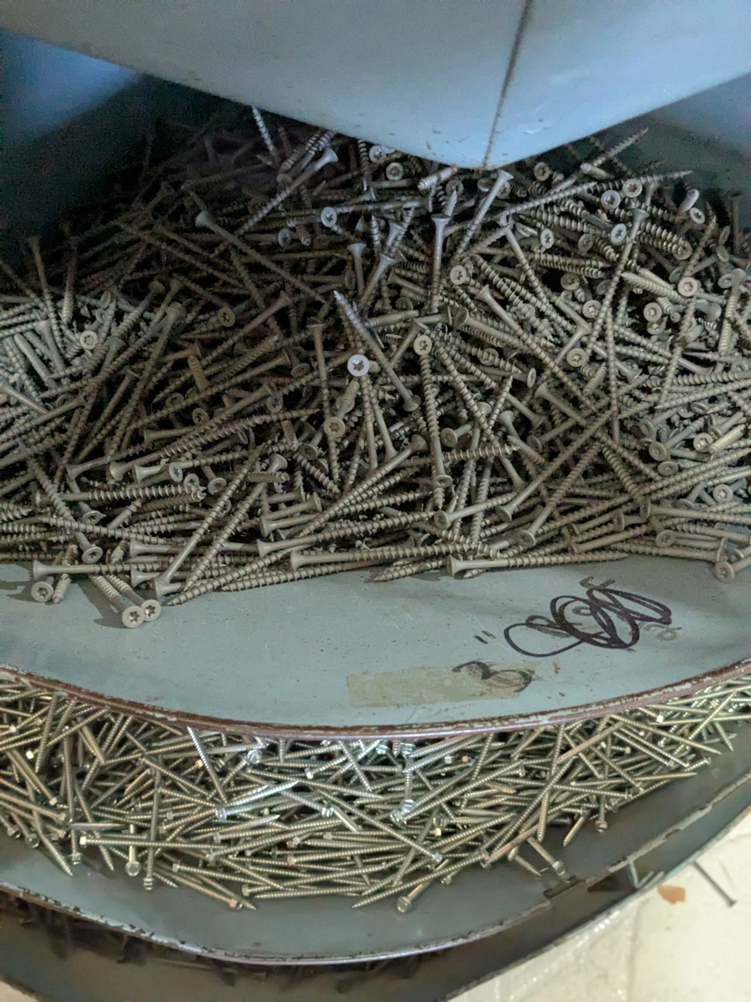 A metal container filled with numerous silver screws of various lengths.