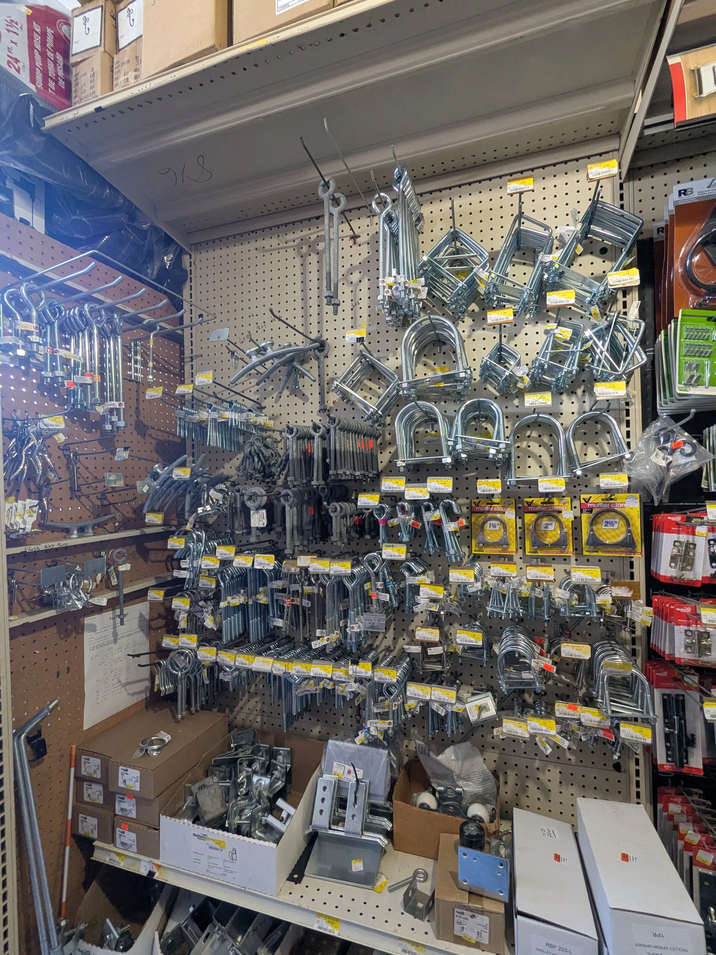 Different types of metal hardware, locks, and small tools arranged on a pegboard in a hardware store.