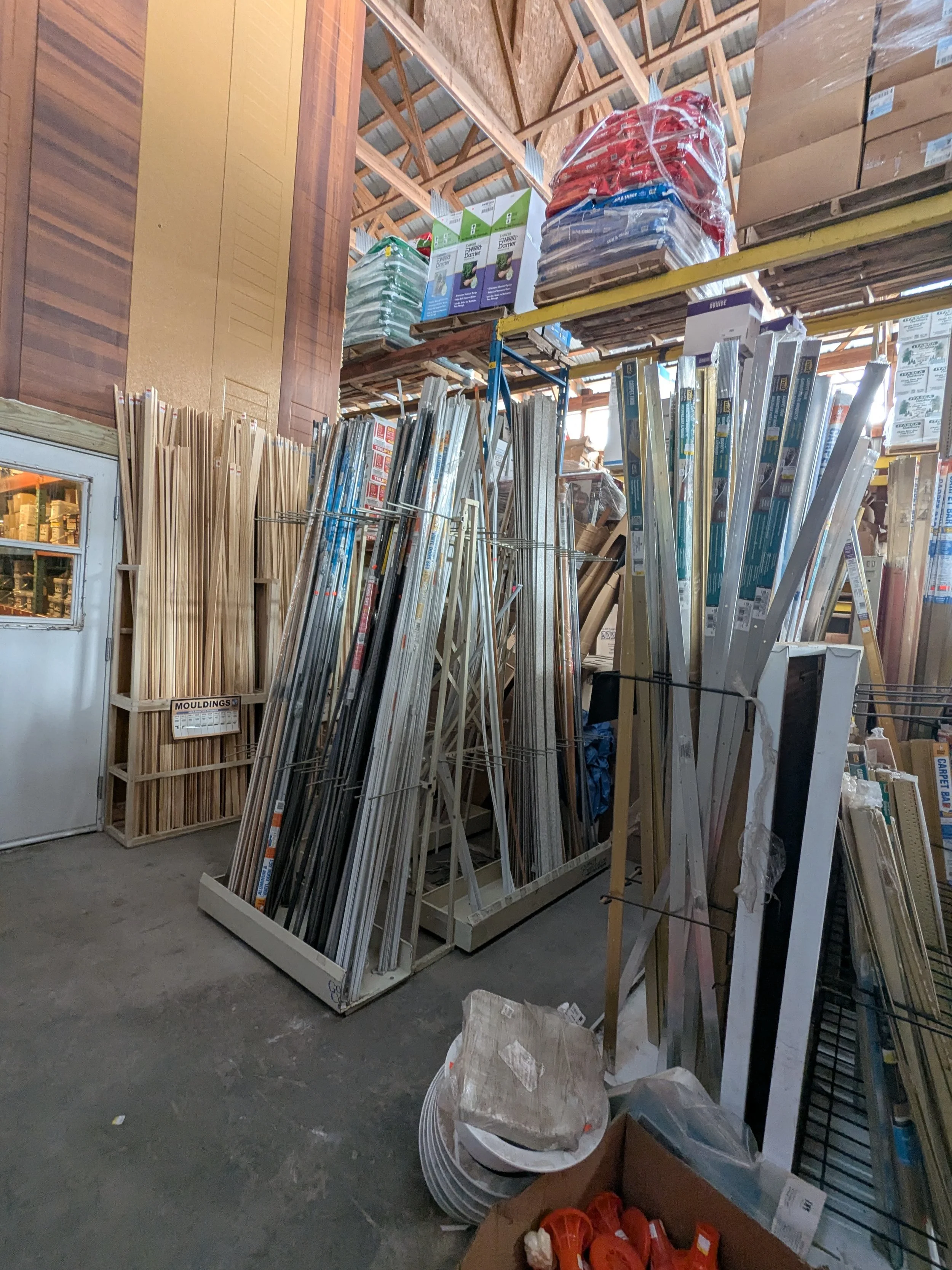 Hardware store aisle with metal rods, wood molding, and shelving products on display.