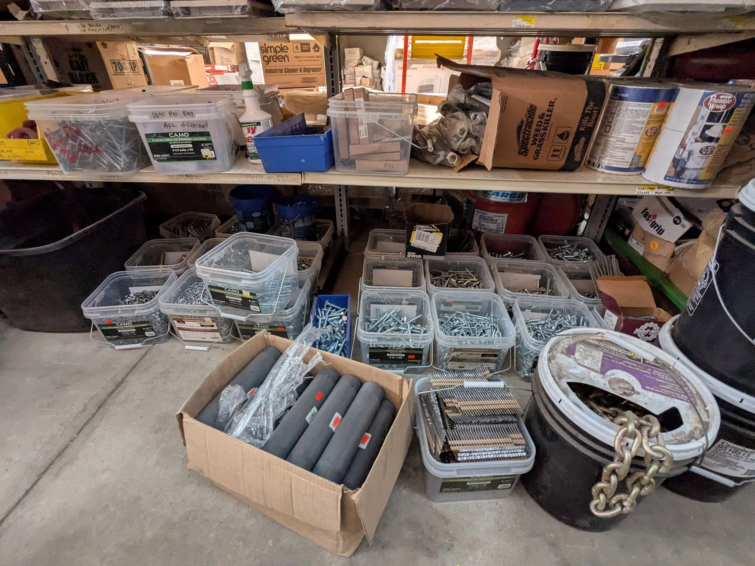 A storage area with shelves holding bins and boxes filled with hardware items like screws, nails, and tools.