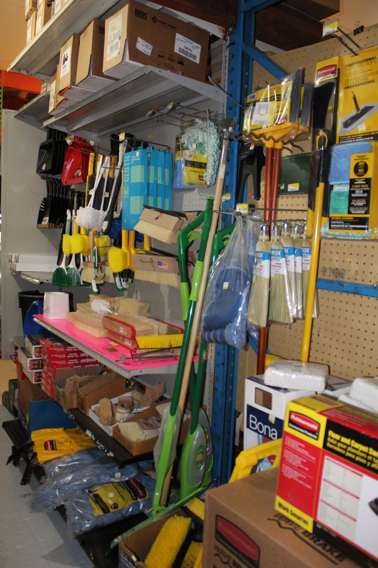 Store display with cleaning tools and supplies including mops, brooms, scrub brushes, and cleaning cloths on shelves and pegboards.
