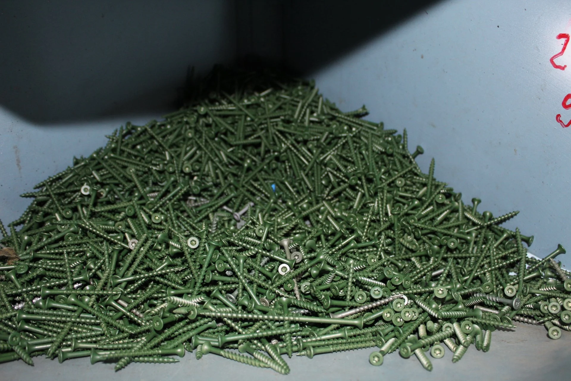 A large pile of green screws on a gray surface in a workshop or storage area.