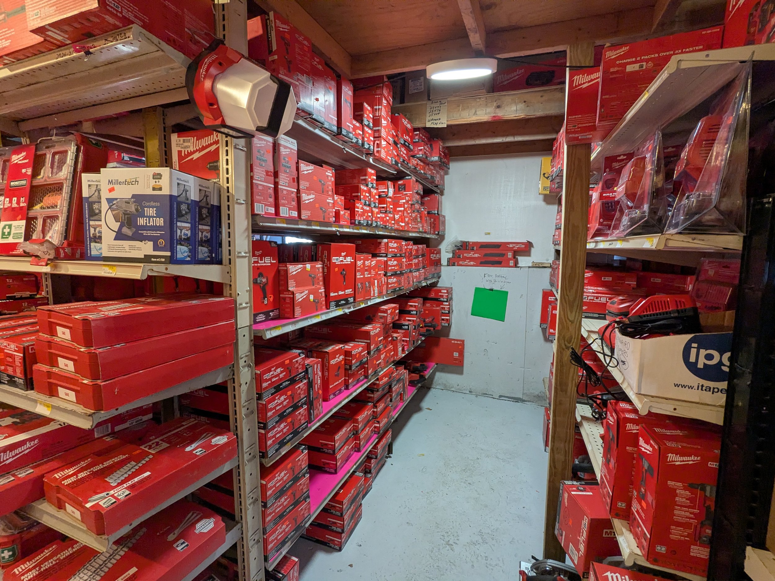 A storage room with shelves filled with red power tools and accessories, including Milwaukee and Millertech boxes, a cordless tire inflator, and other power tool equipment.