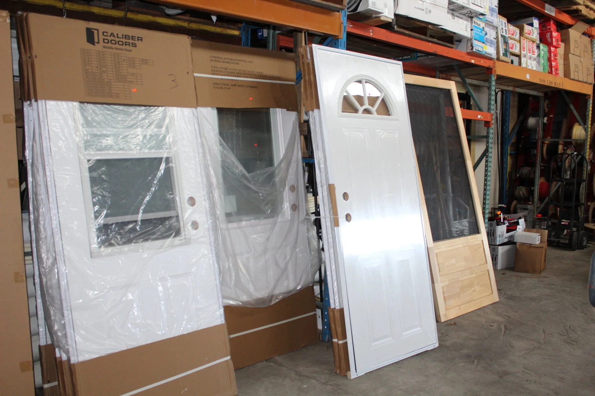 Store display with various doors, including a white door with an arched window, a door with a glass panel, and a wooden door, leaning against a shelving unit.