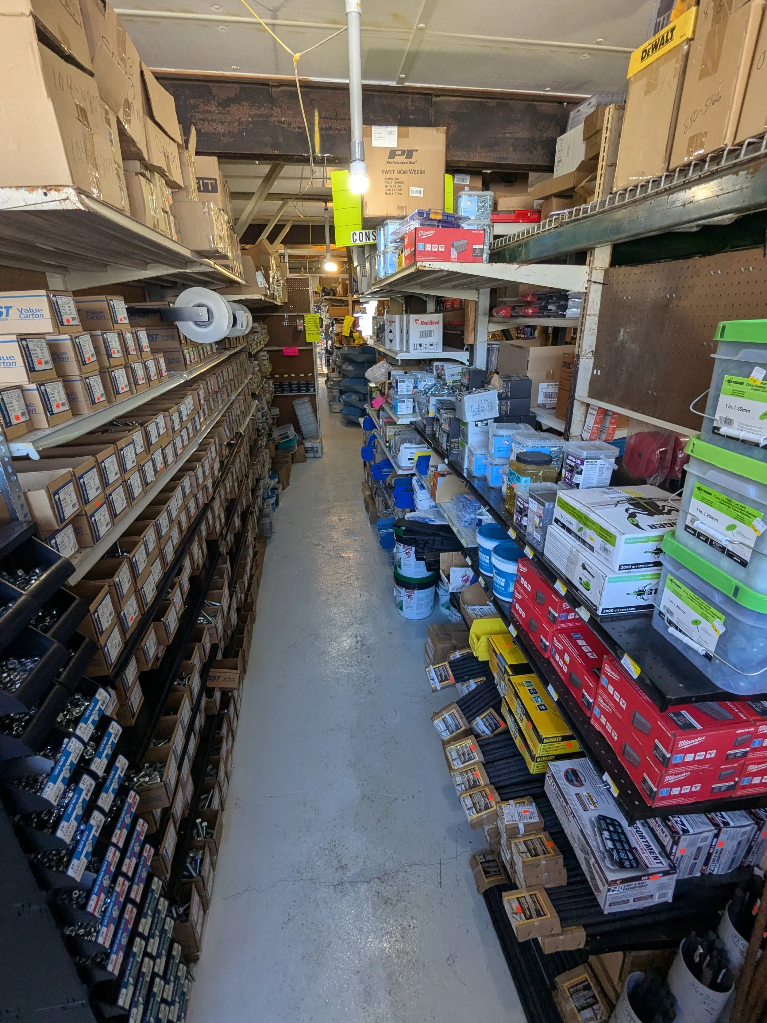 A narrow aisle in a hardware store with shelves stocked with boxes of various tools and supplies.