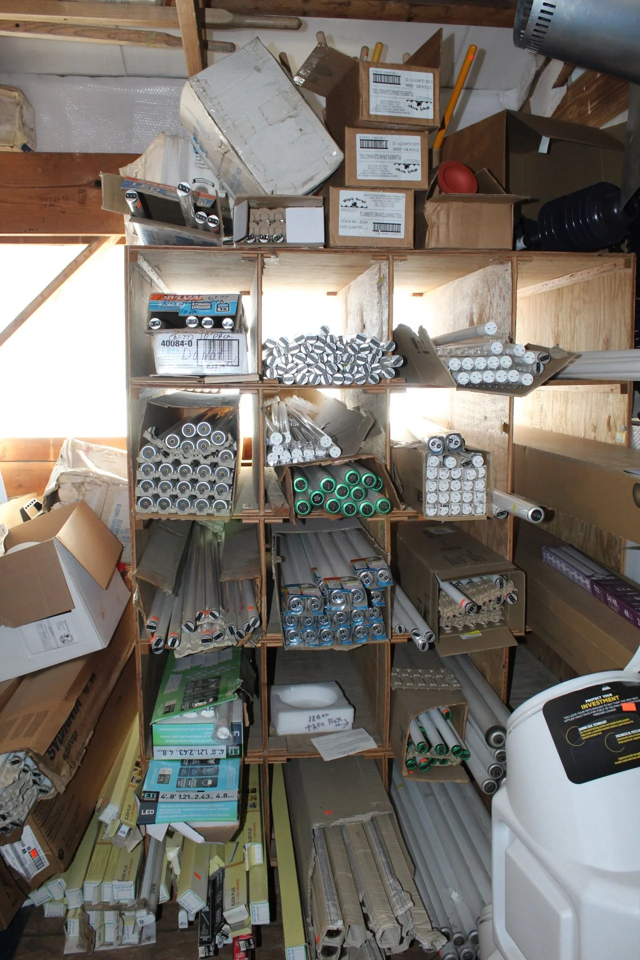 Shelving unit filled with various rolls of aluminum foil, plastic wrap, and other packaging materials, with boxes and storage items surrounding it.