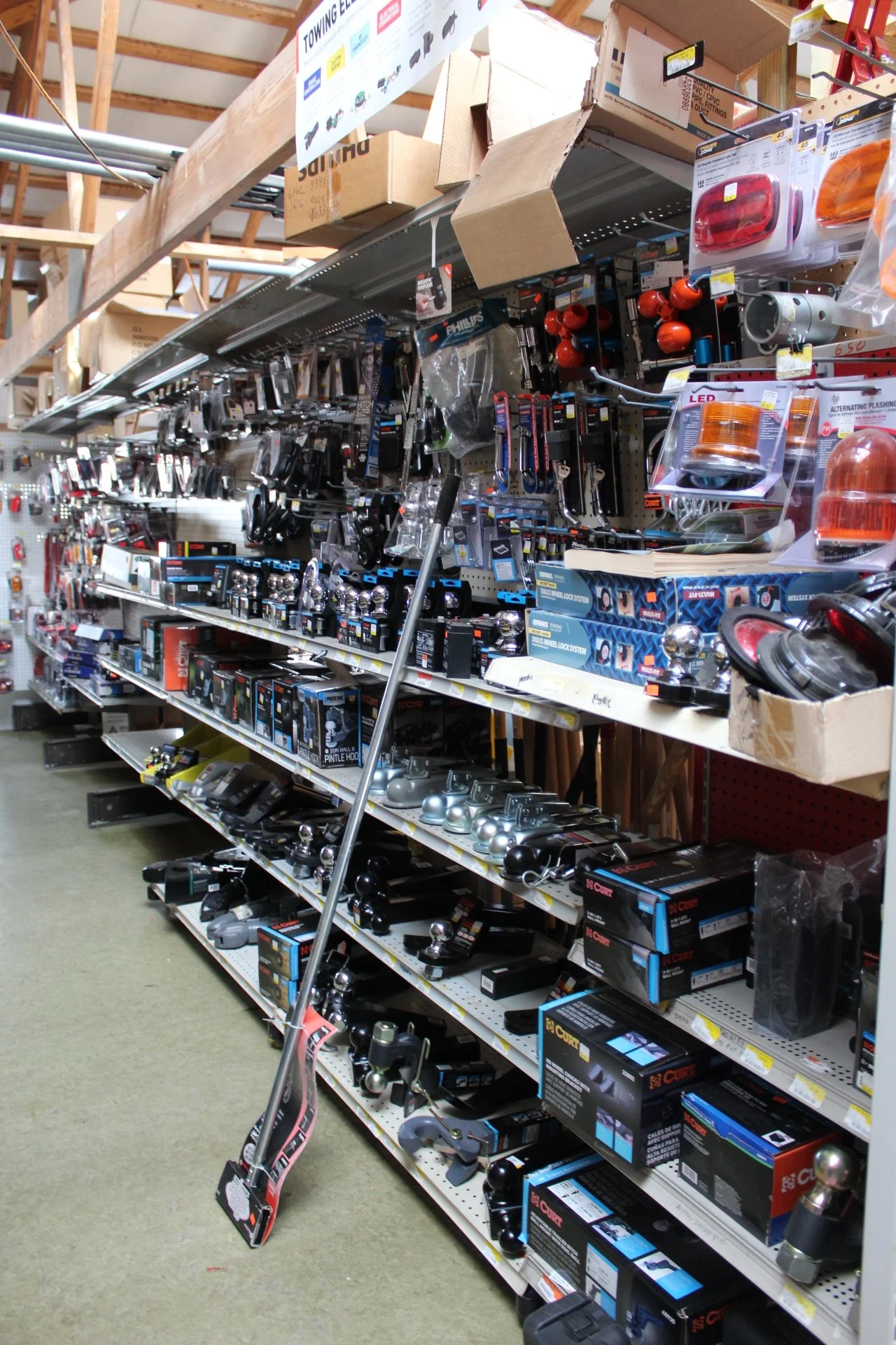 A aisle in a hardware store shelf stocked with vehicle towing equipment, such as ball hitches, lock system, and other accessories.