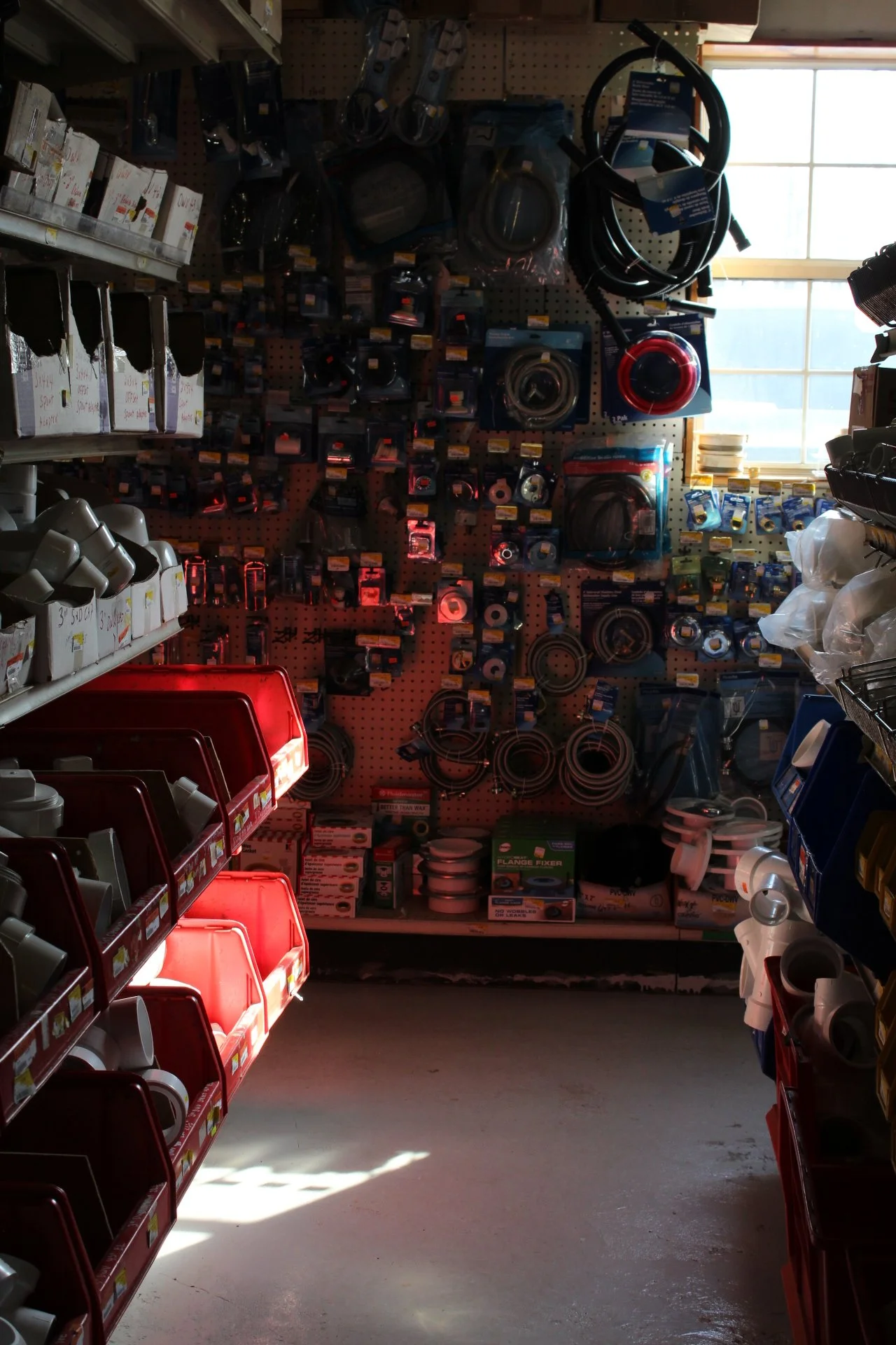 Store aisle with shelves containing plumbing supplies like hoses, fittings, and other hardware items.