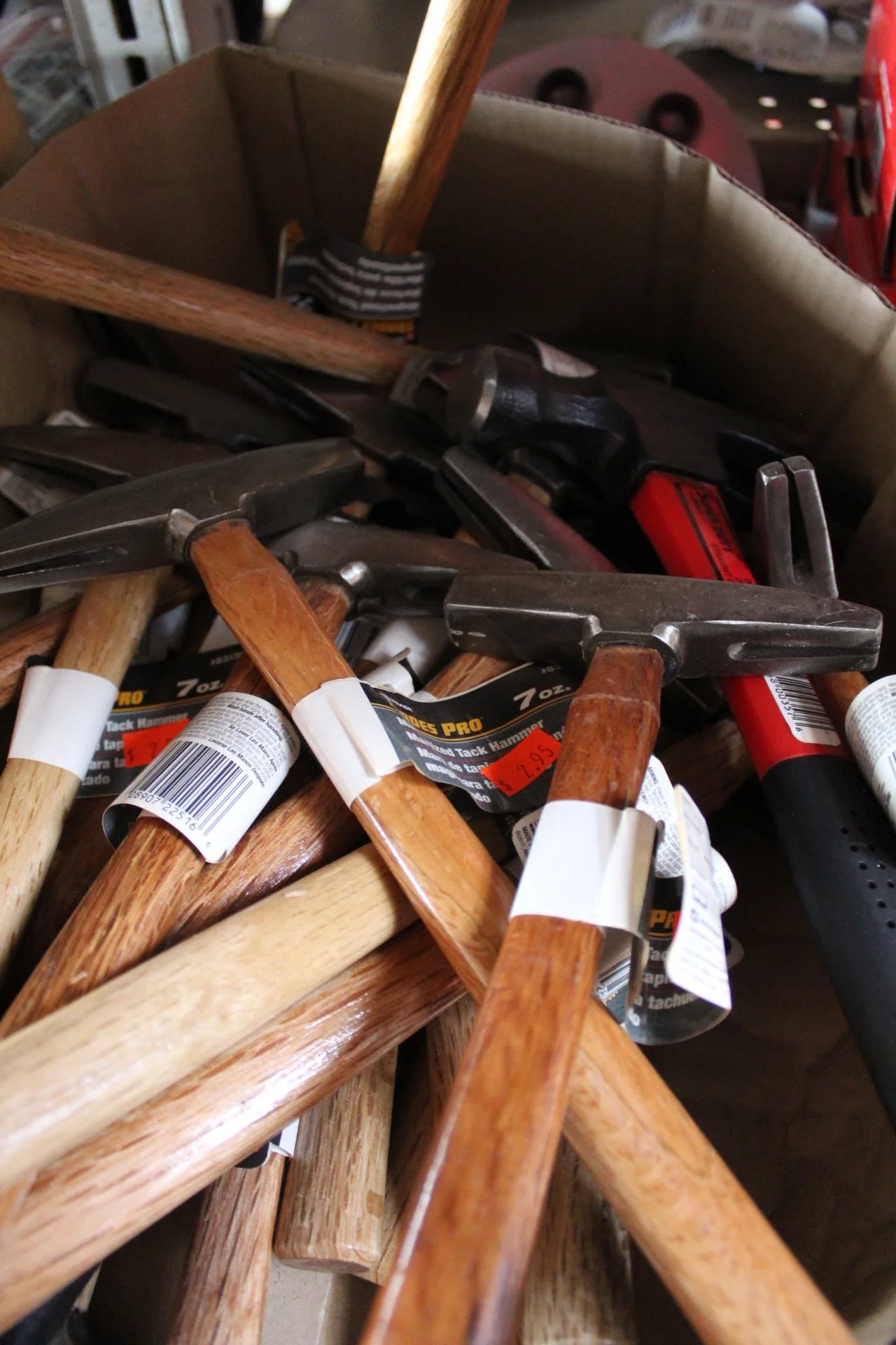 A pile of hammers with wooden and metal handles in a storage area or workshop.