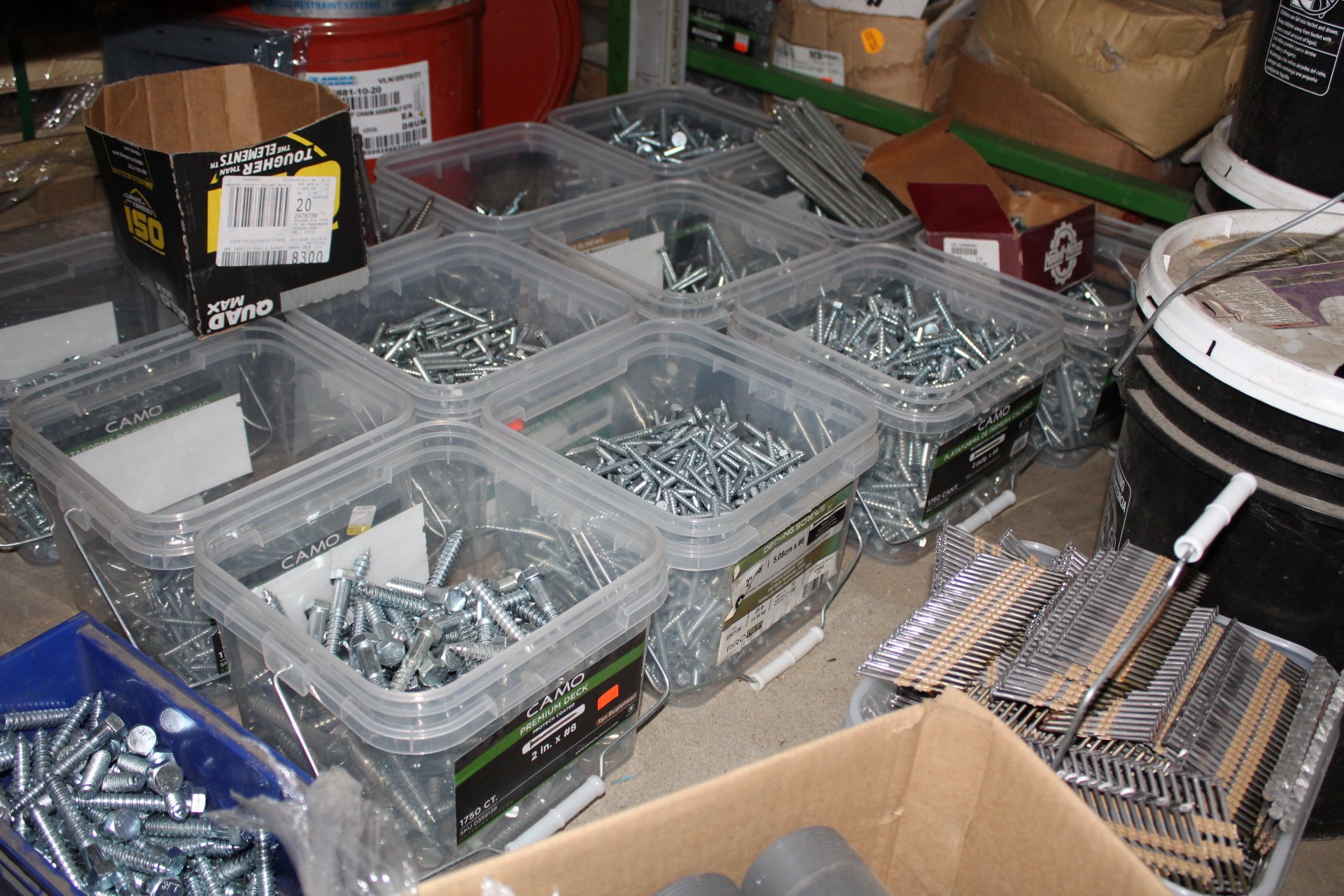 Assorted hardware screws, nails, and other fasteners organized in clear plastic storage containers on a workbench.
