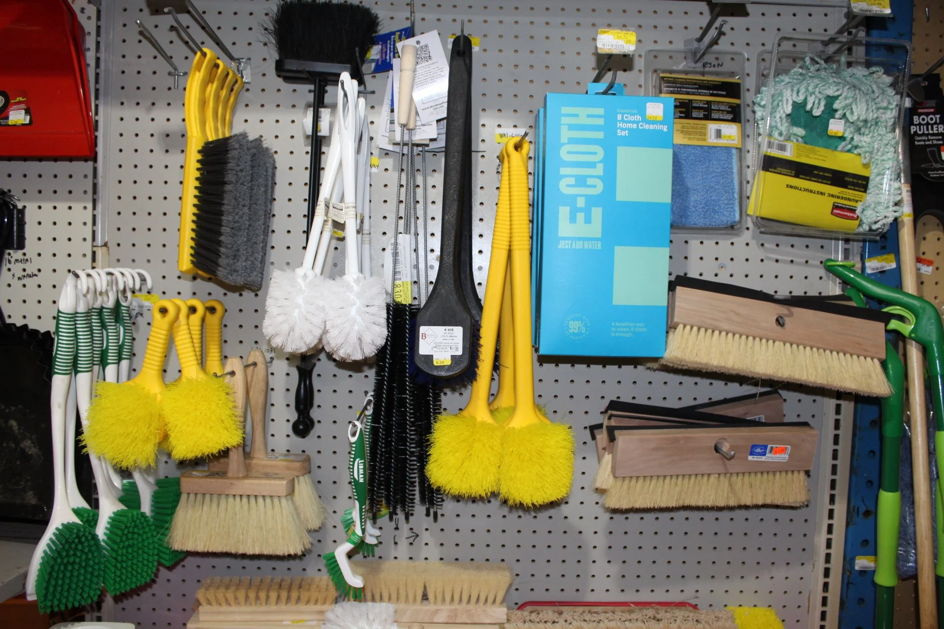 A collection of cleaning brushes, scrubbers, and cleaning tools hanging on a gray pegboard display in a hardware store.
