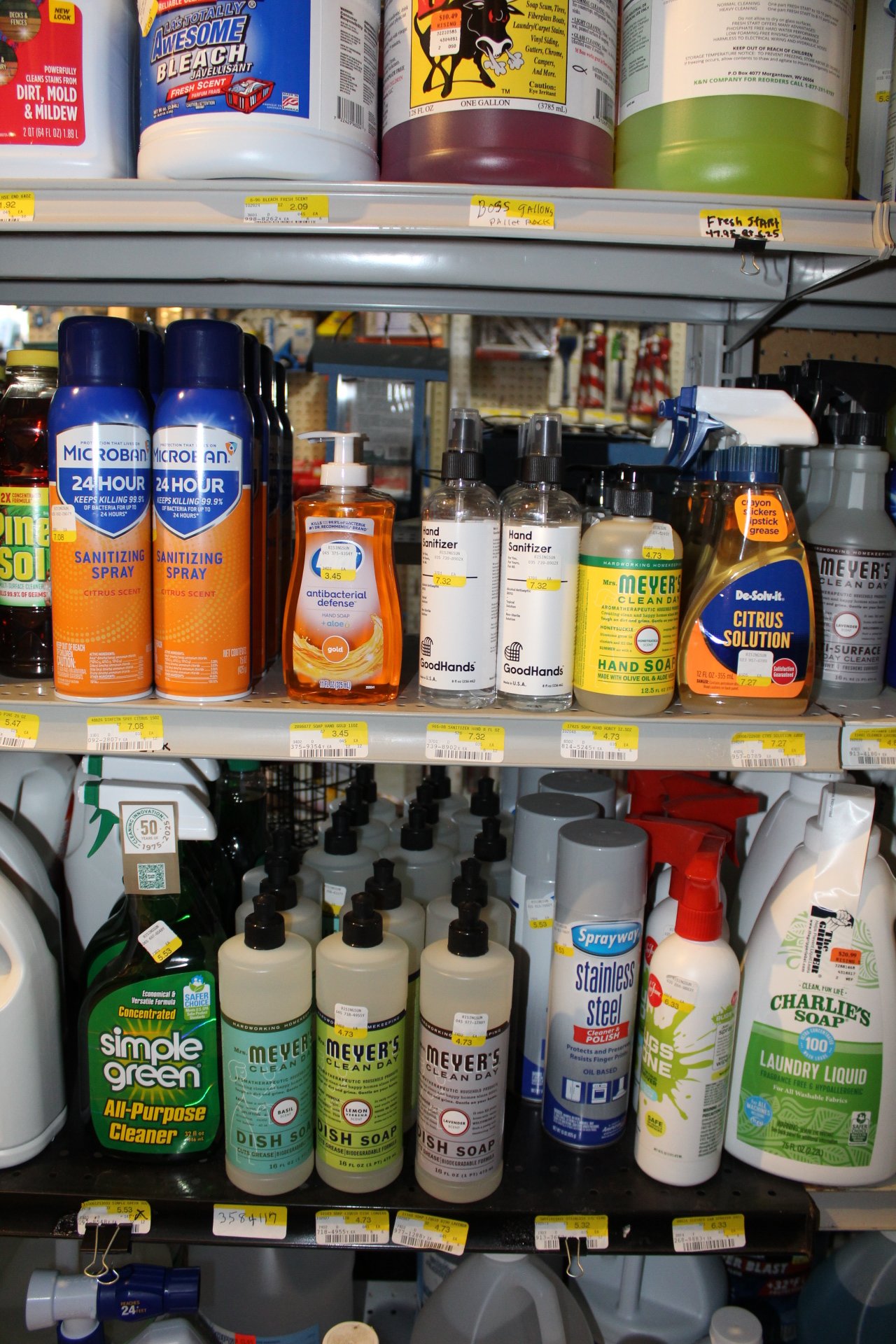 Shelf with various cleaning and sanitizing products including spray bottles, hand sanitizer, dish soap, and laundry liquid.