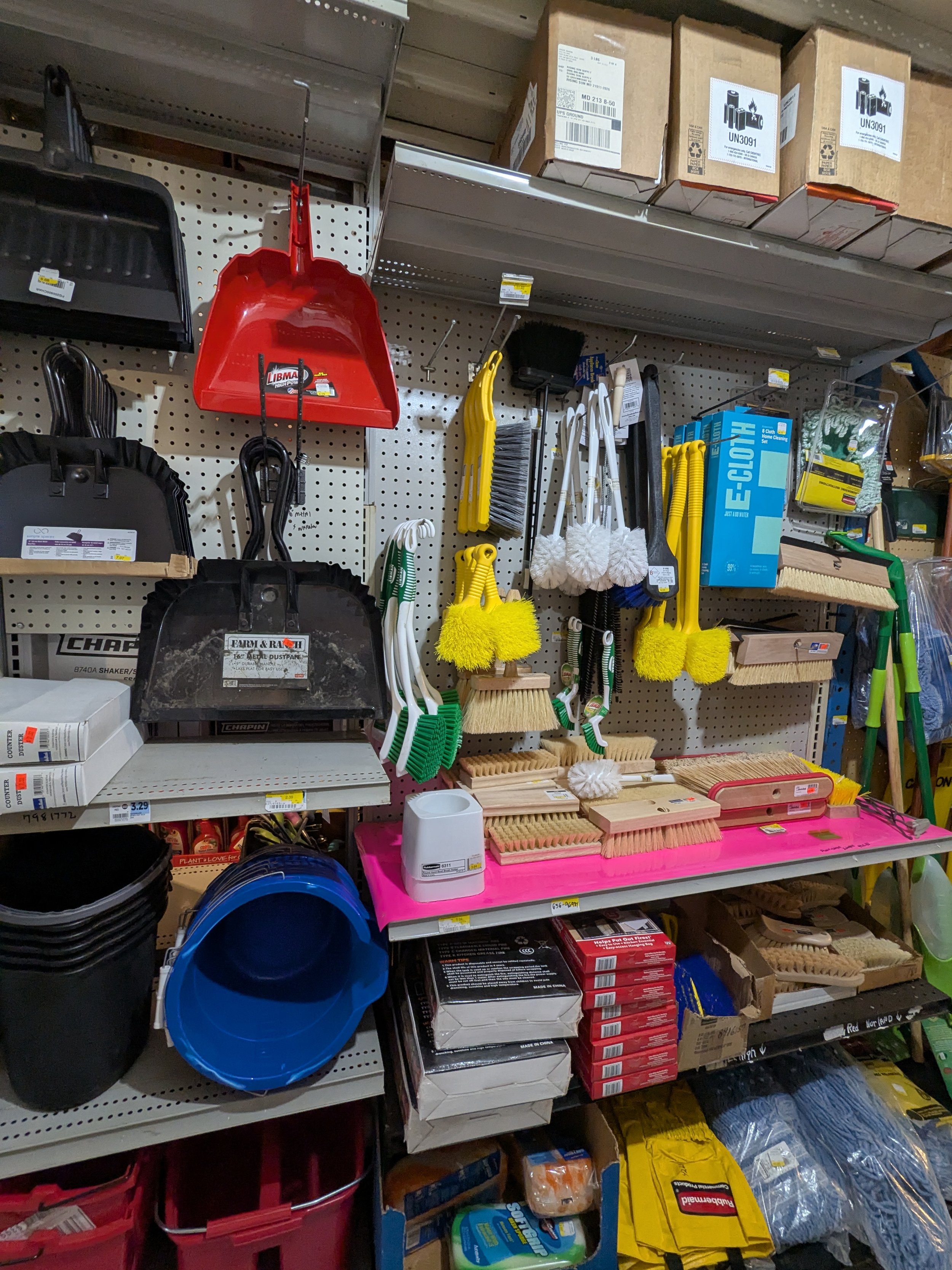 Display of cleaning supplies, including dustpans, brushes, scrubbers, buckets, and cleaning gloves on a store shelf.