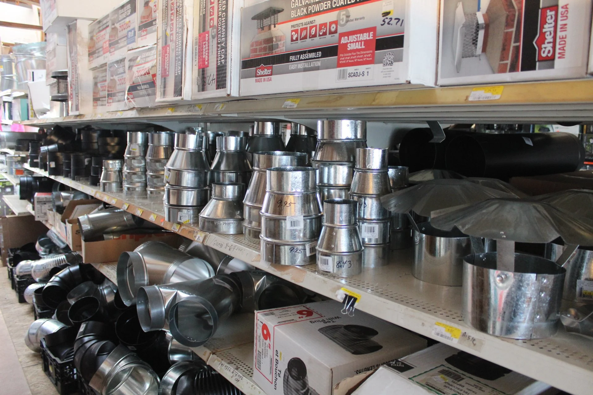 Metal chimney and vent pipe fittings on store shelves in a hardware store aisle.