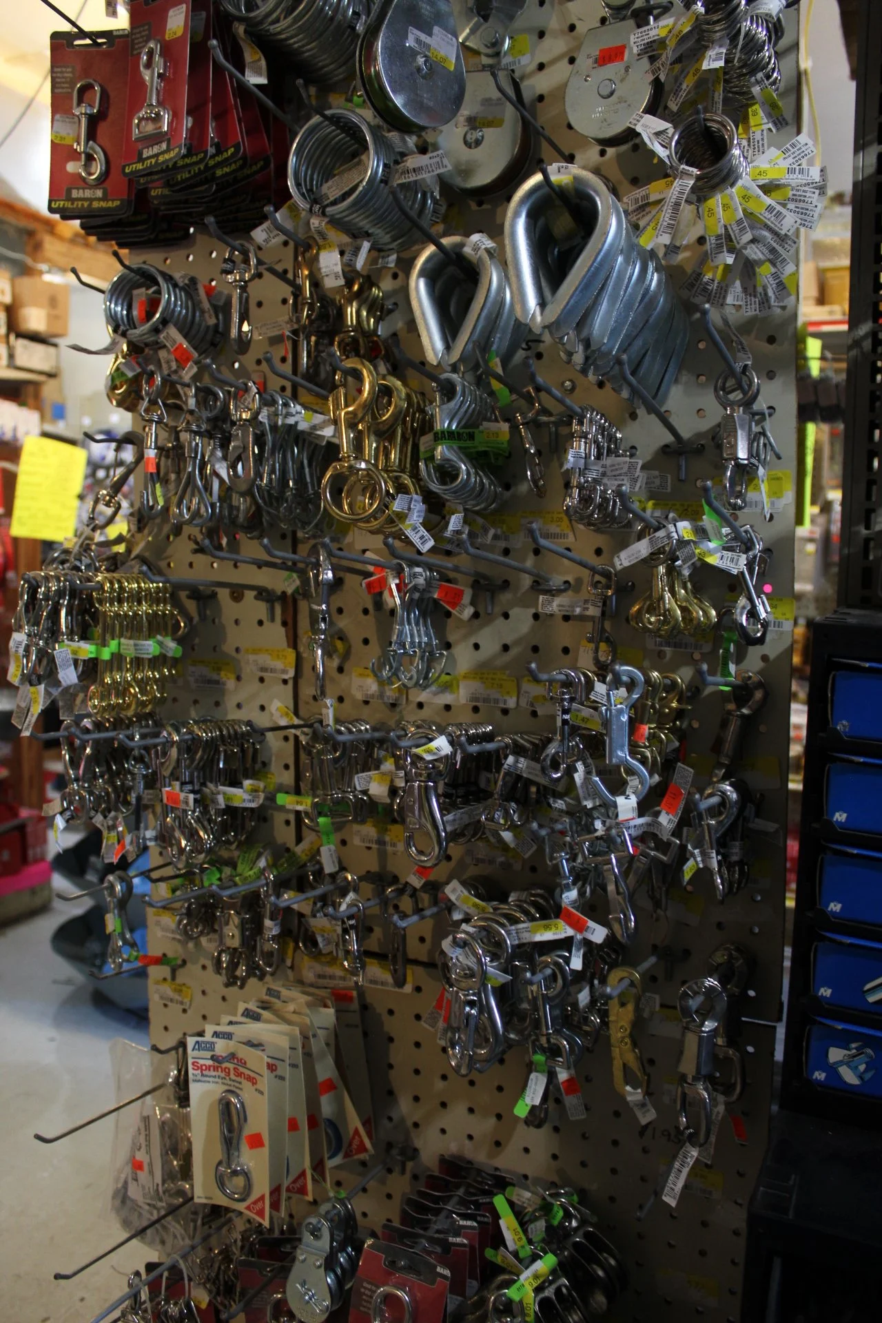 Display of various metal hooks, keys, and latch parts hanging on a pegboard in a hardware store.