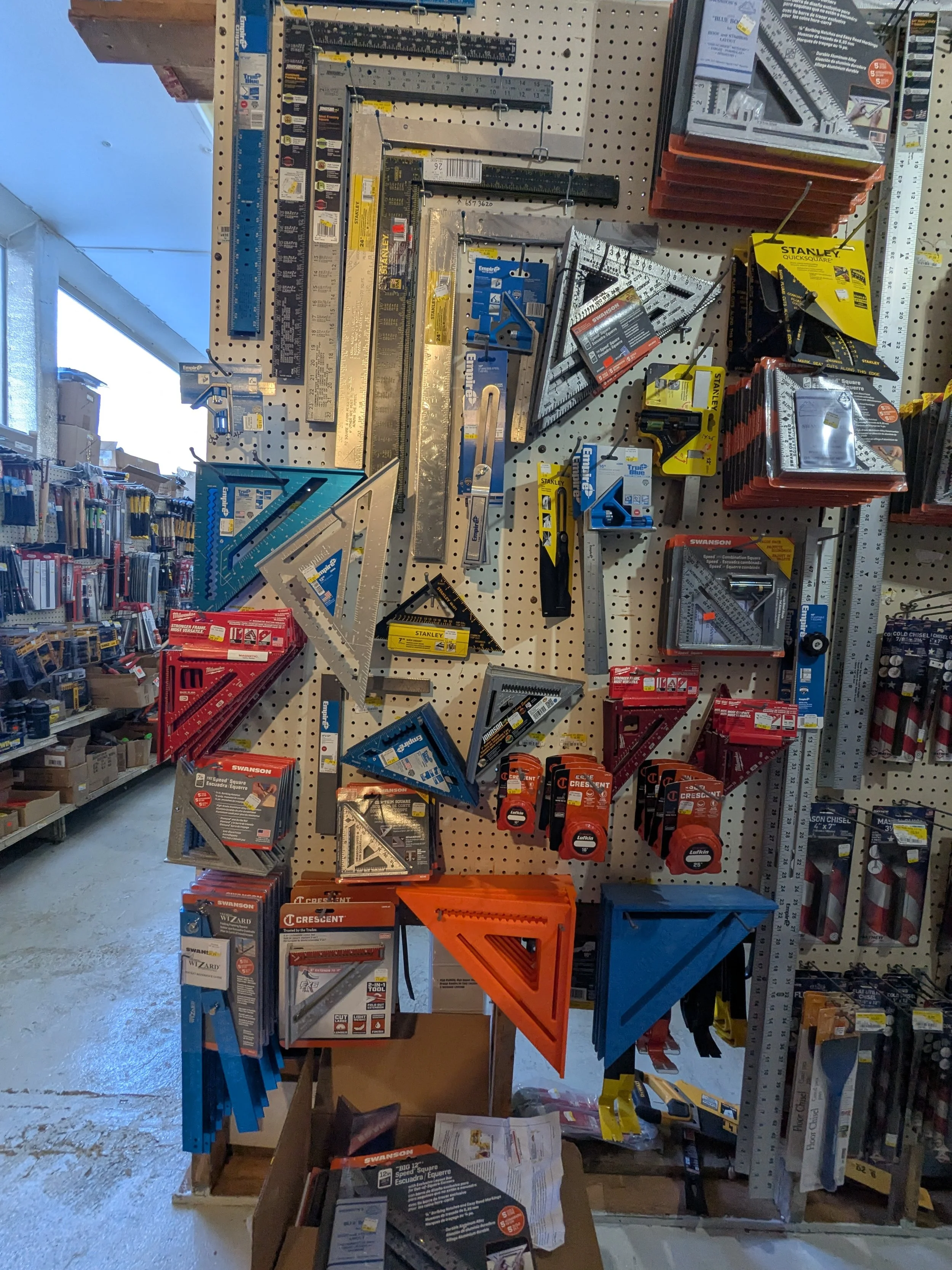 Display of various measuring tools including squares, rulers, levels, and protractors on a pegboard at a hardware store.