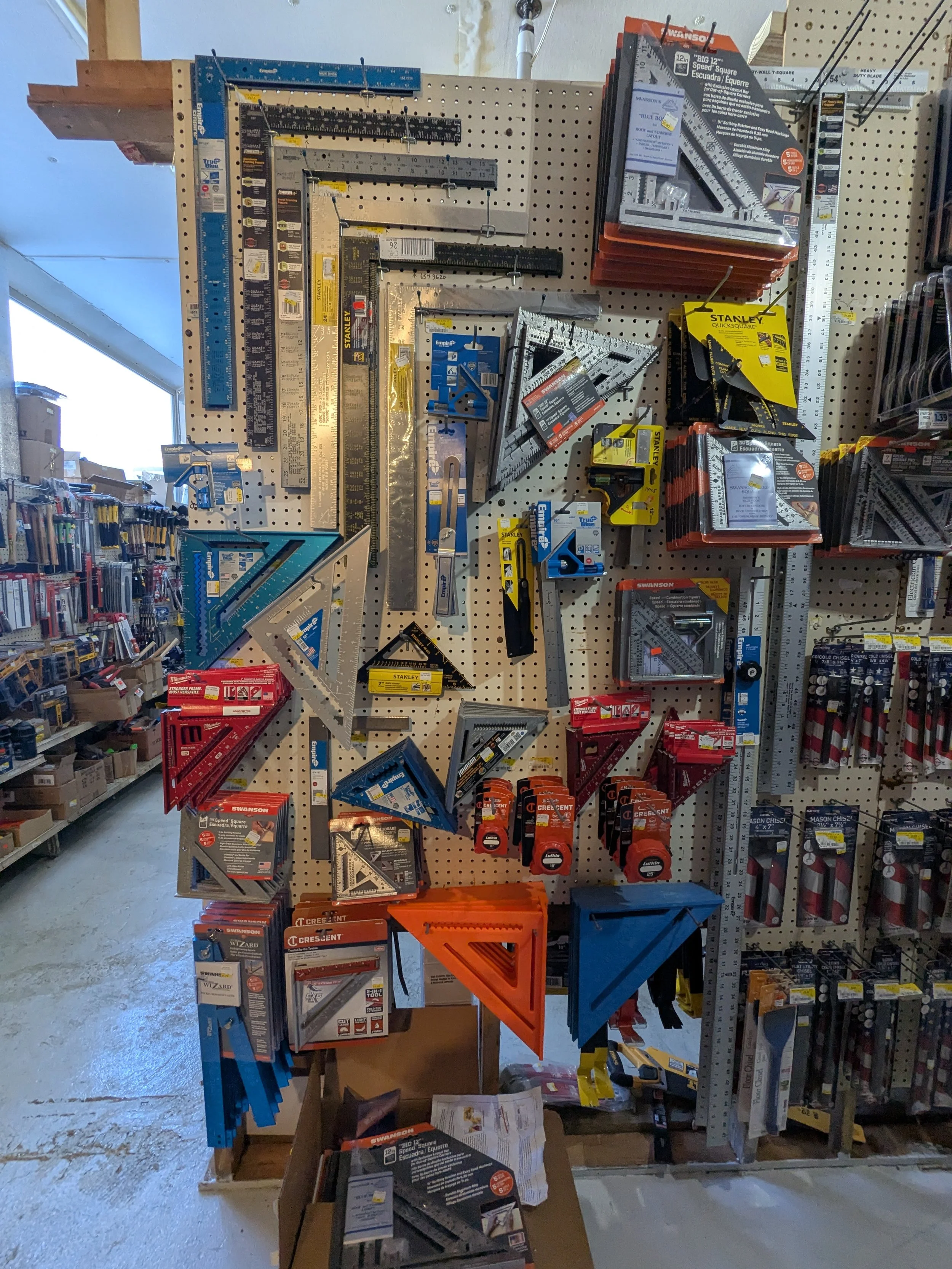 Display of various measuring tools including squares, rulers, and levels hanging on a pegboard at a hardware store.