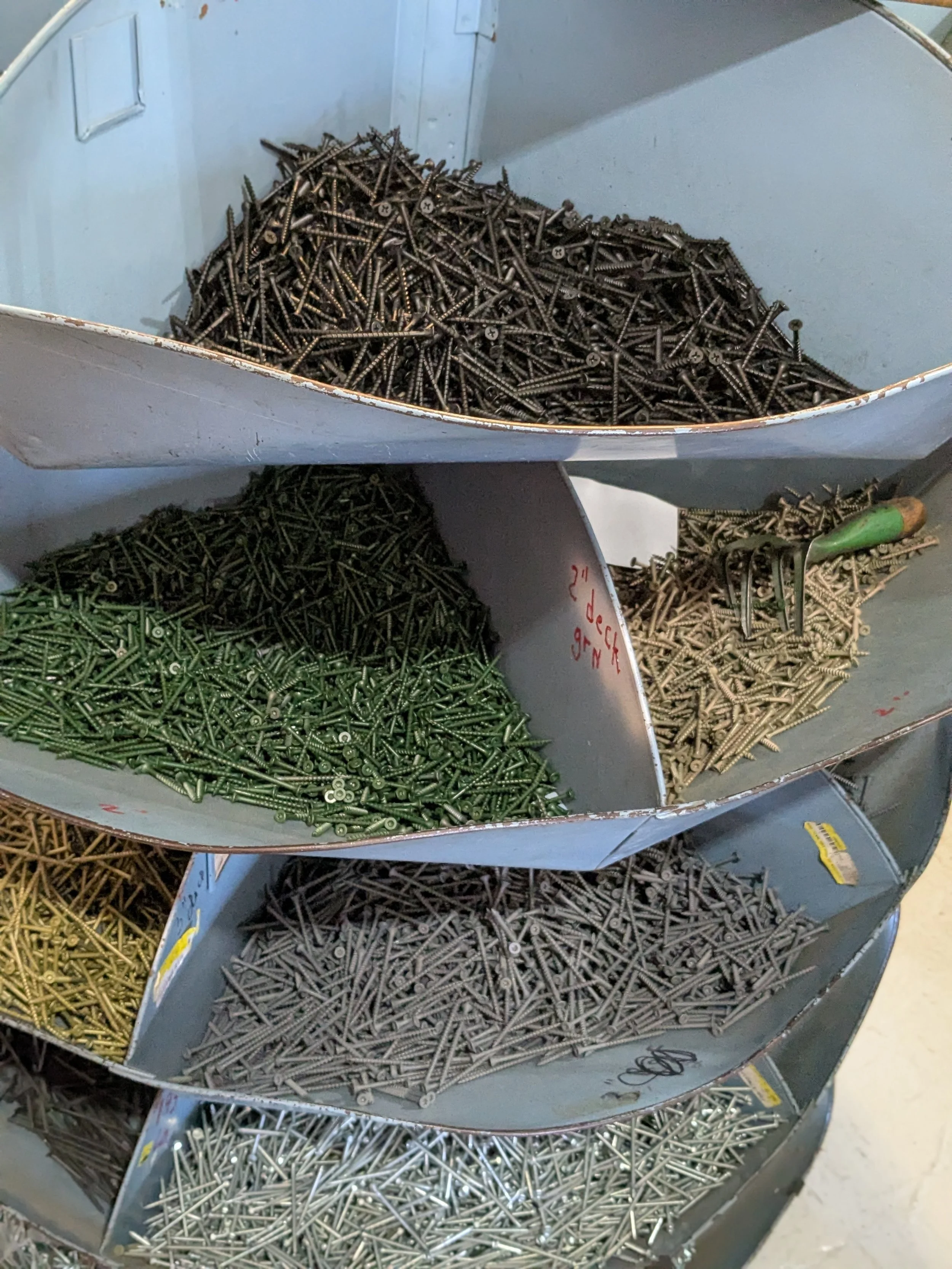 Multiple compartments filled with different colored screws, including black, green, silver, and brass-colored, stored in a metal organizer.