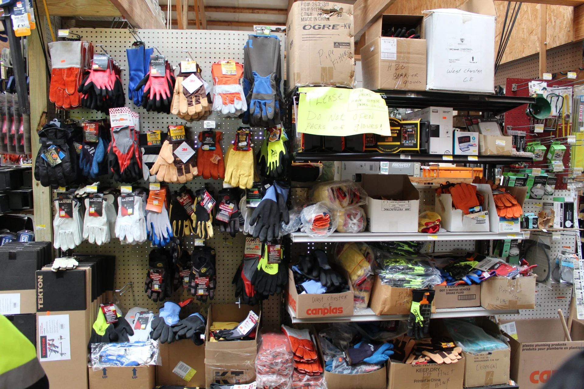 Store shelf with gloves, boxes, and tools, along with a yellow sign that reads 'PLEASE Do Not Open PACKS of gloves!'