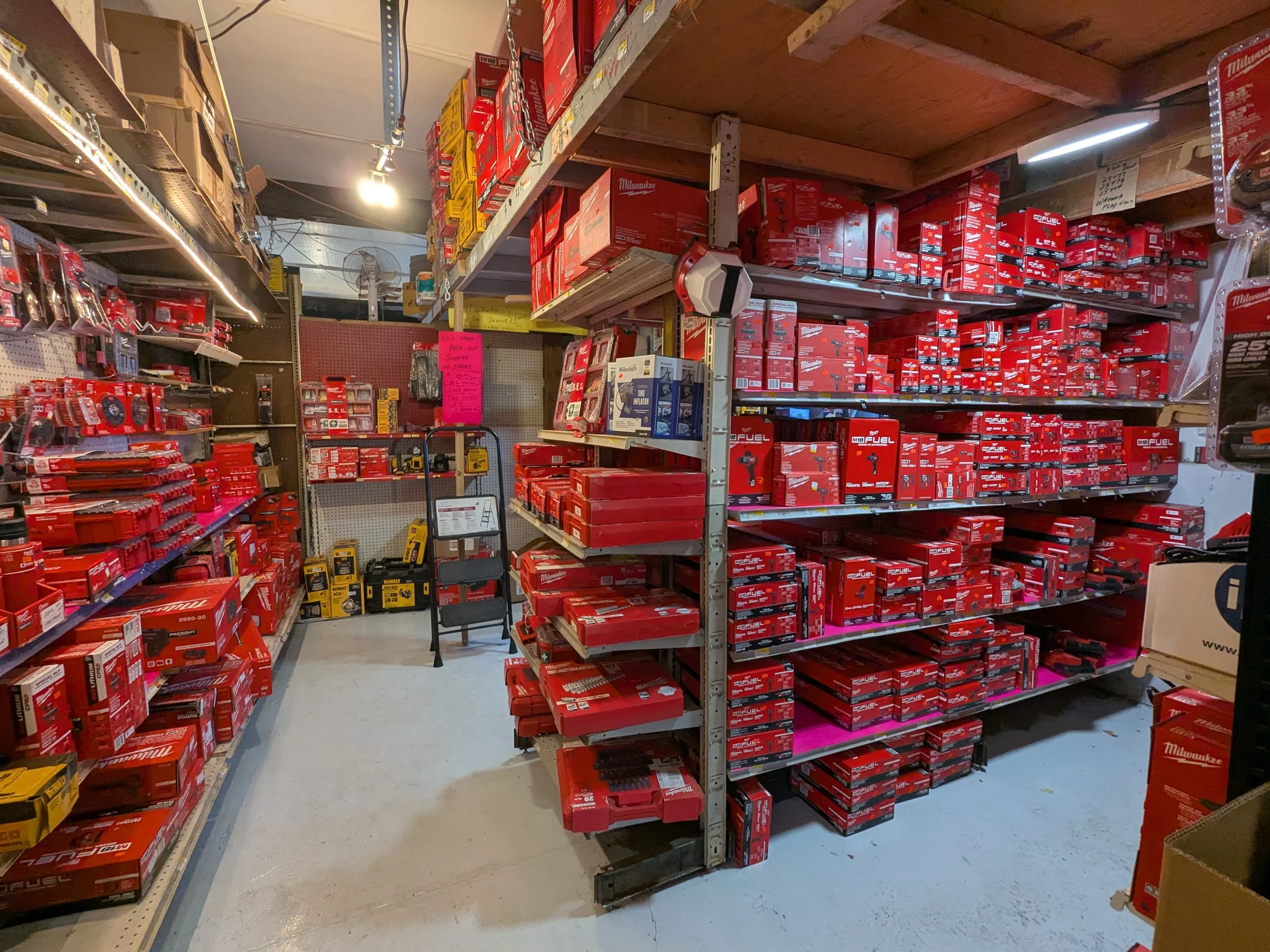A hardware store aisle filled with red Milwaukee power tool boxes and packages on metal shelves.
