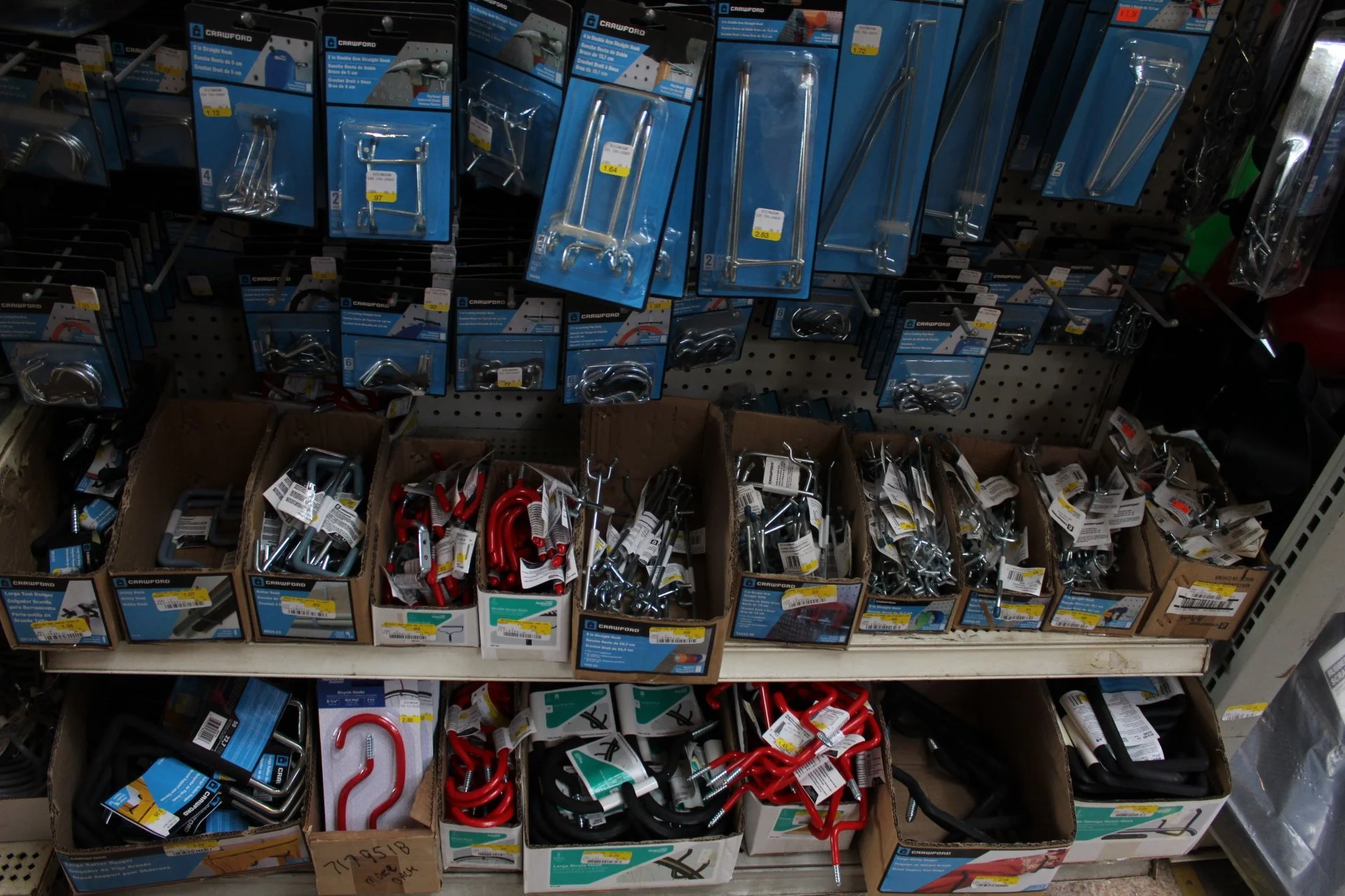 Display of various hardware hooks and holders in retail store, arranged in cardboard boxes and hanging on pegboards.