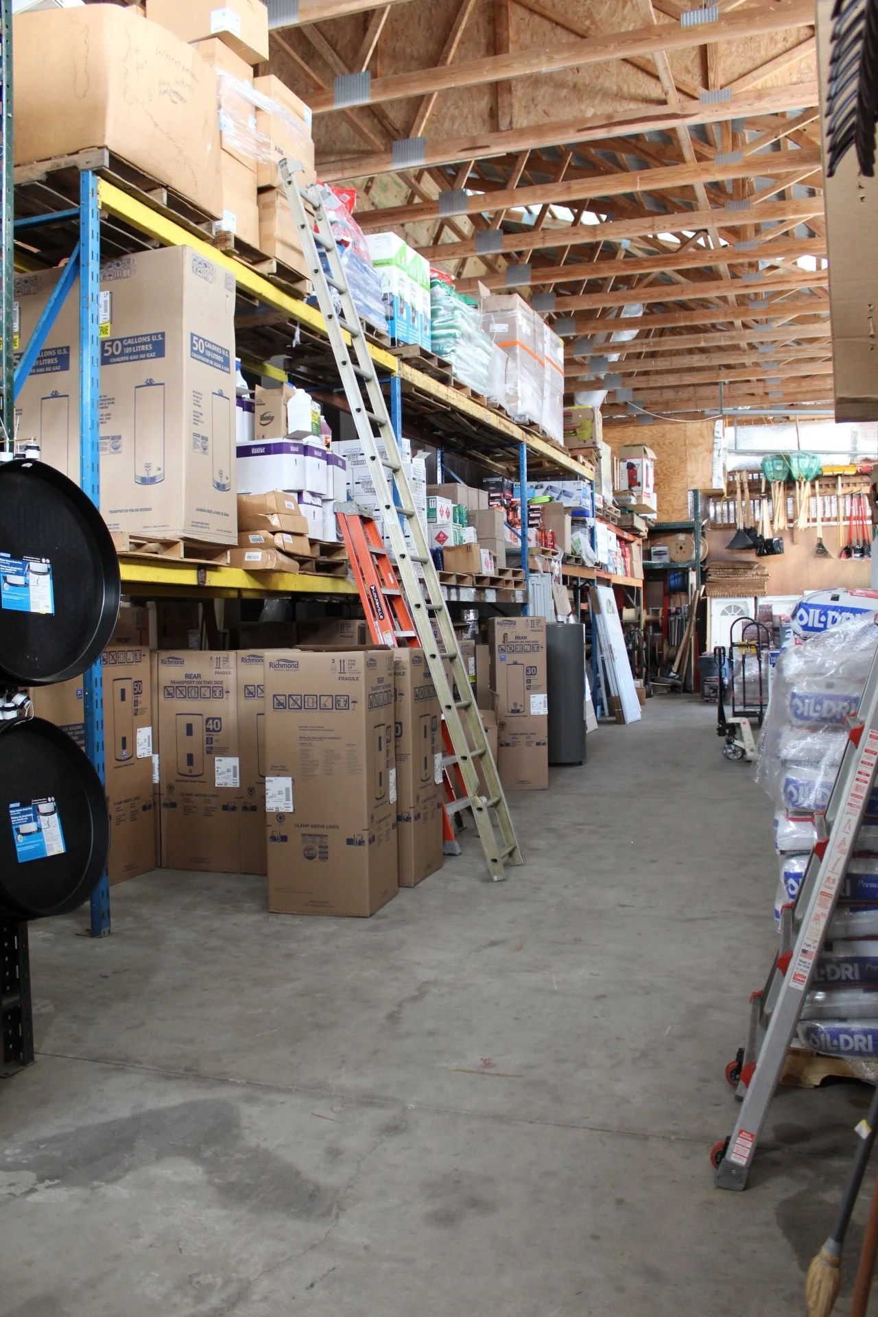 Shelves stacked with boxes, ladders leaning against them, and various tools and supplies in a warehouse or storage area.
