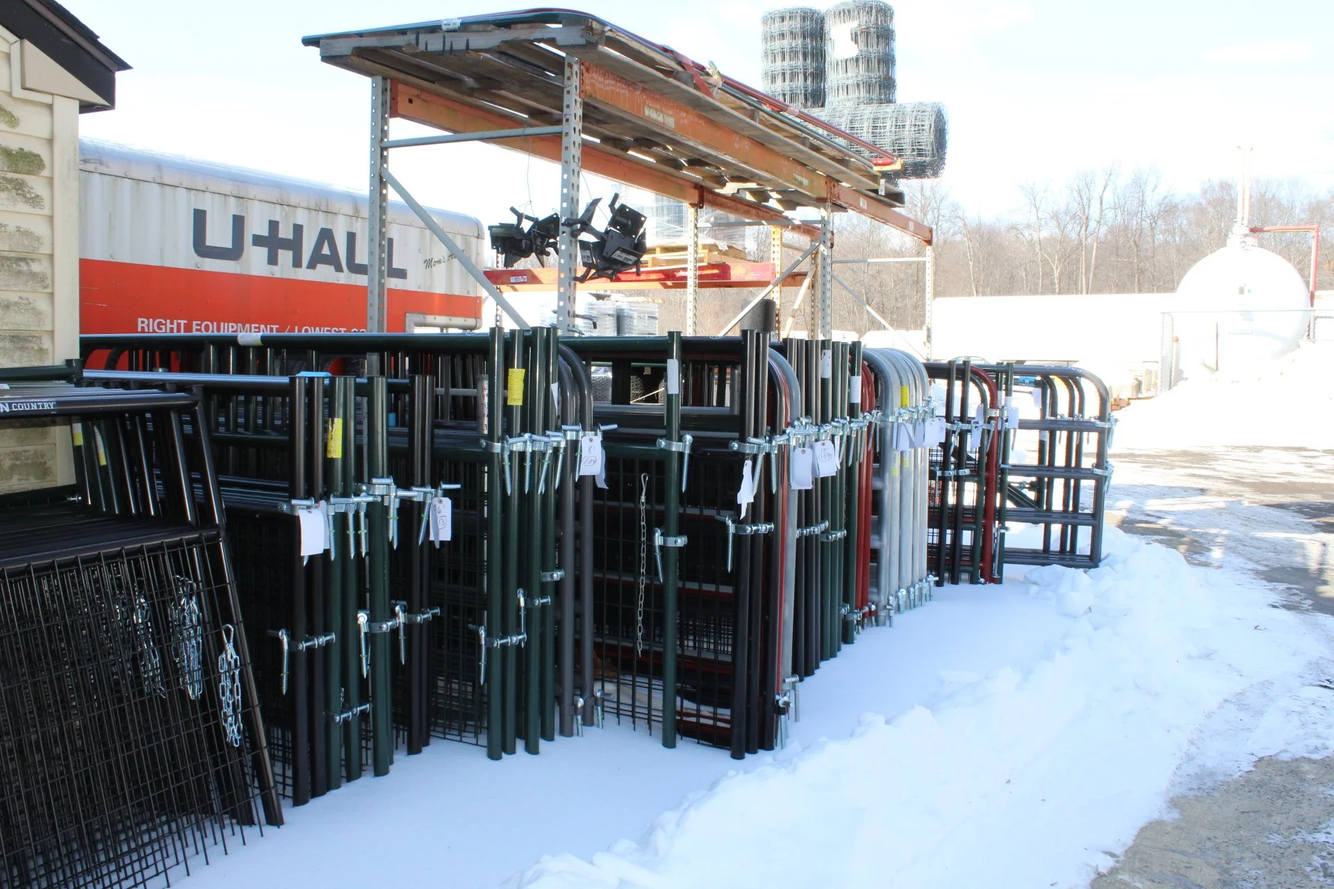 Outdoor storage area with metal carts and fencing panels, snow on the ground, U-Haul truck and storage racks in the background.