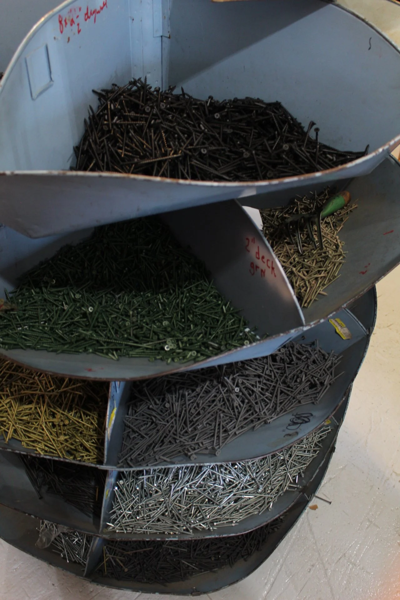 A metal wheel cart with five compartments filled with different types of screws in black, green, gold, silver, and dark grey colors.