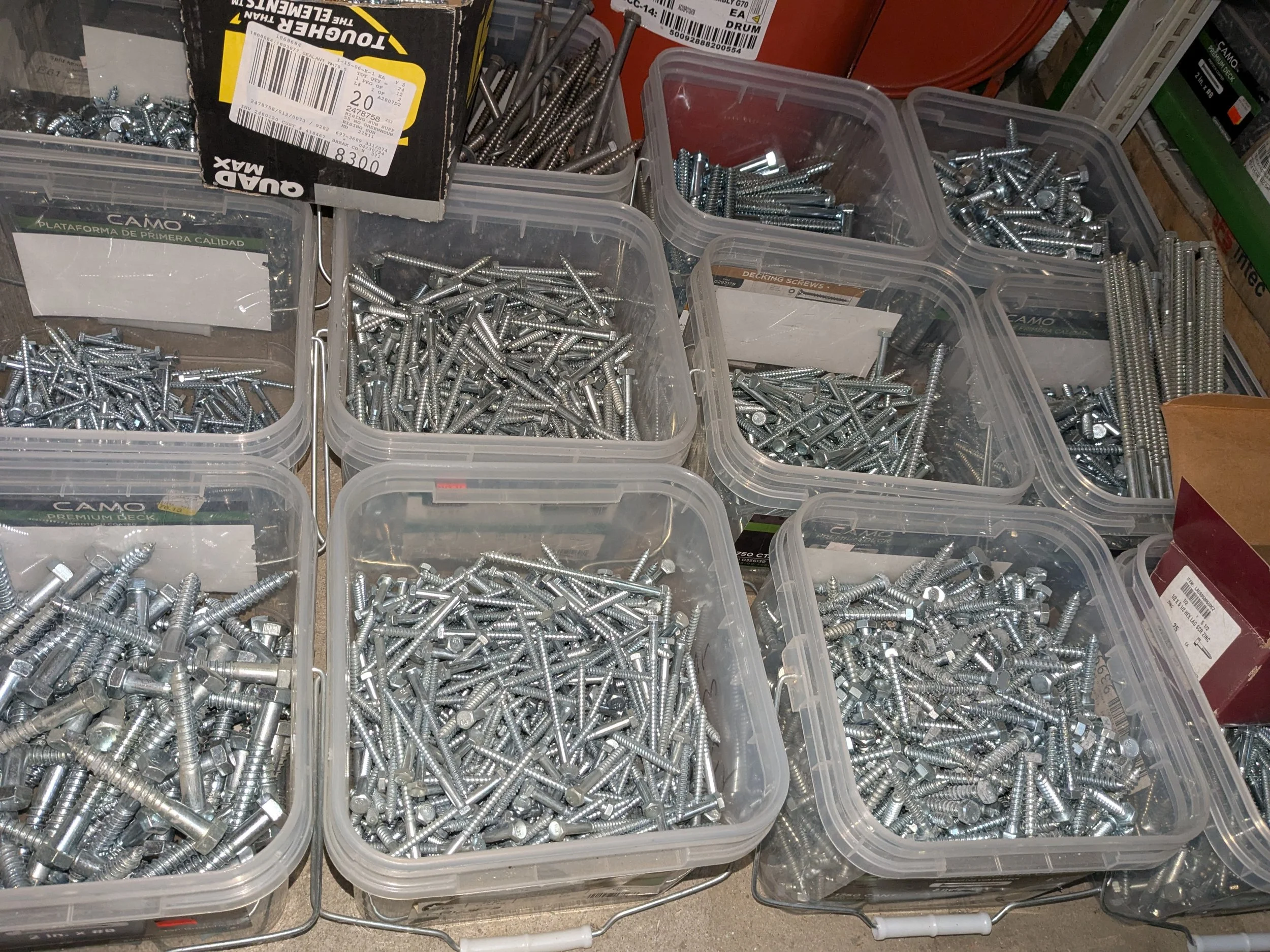 Multiple transparent plastic containers filled with various types of metal screws and bolts on a workbench or display surface.