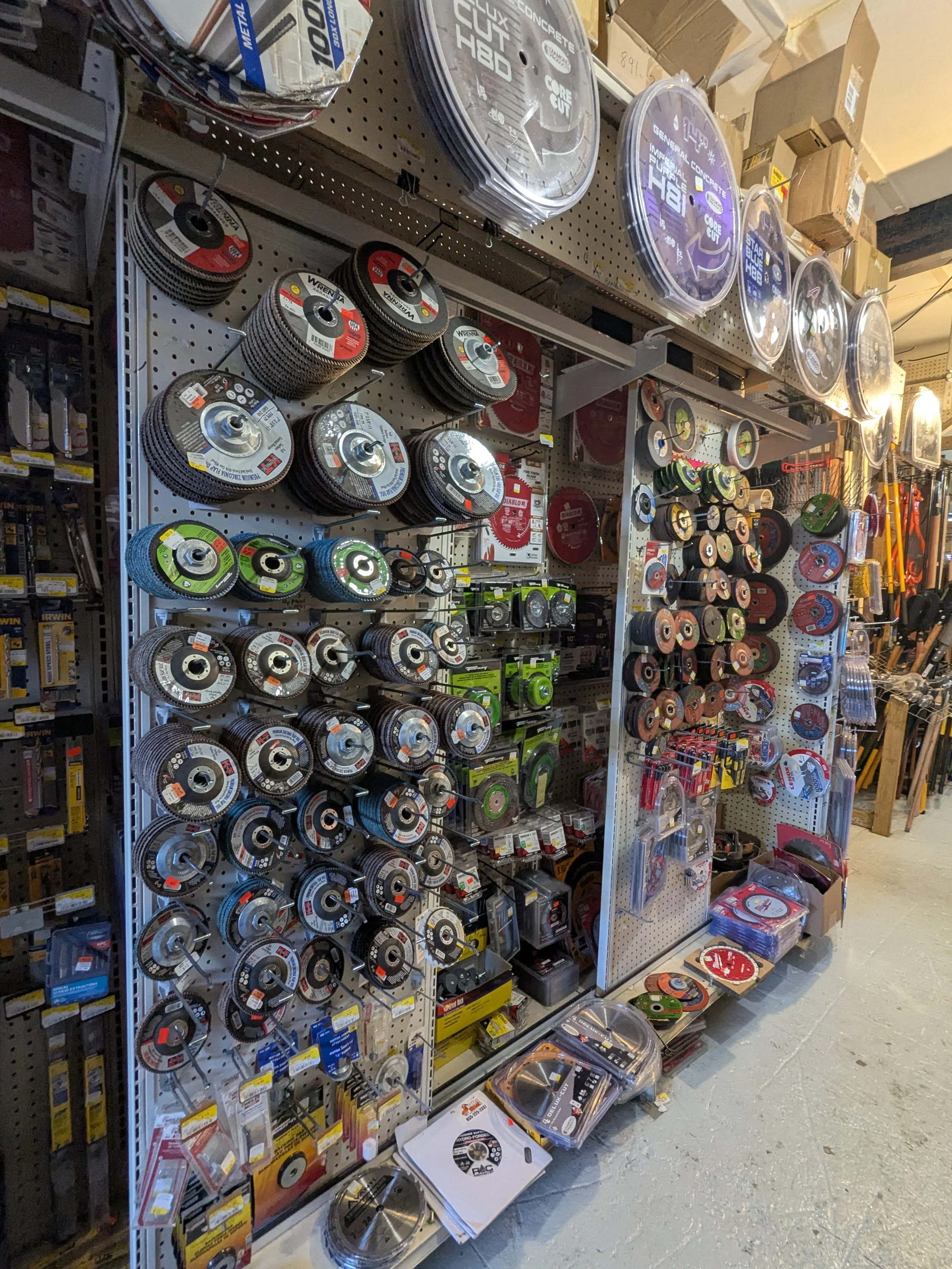 A hardware store aisle displaying a variety of circular saw blades and cutting discs arranged on pegboards and shelves.