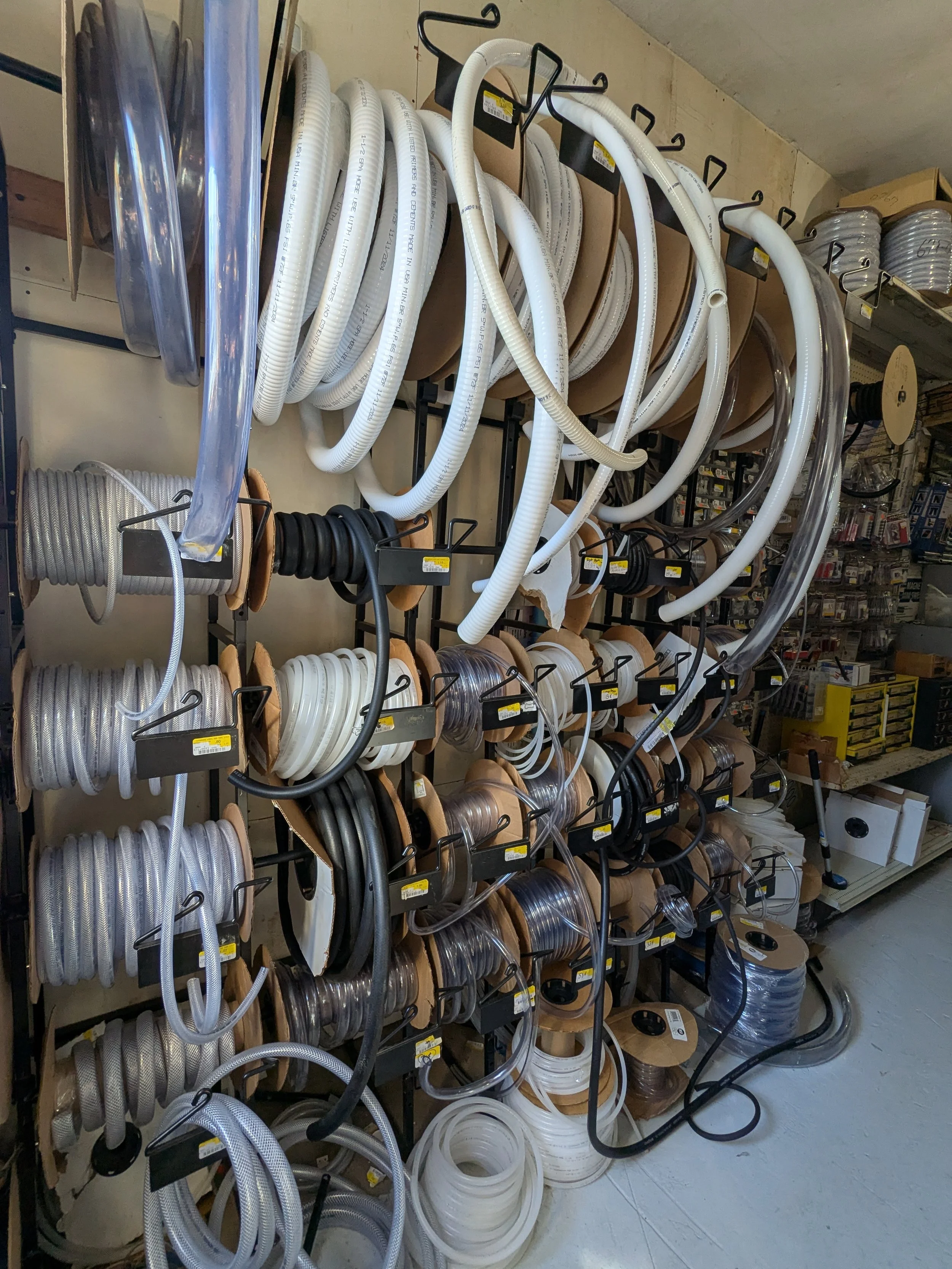 A store shelf filled with various rolls of electrical cables and wires of different colors and sizes, neatly organized on hooks and spools.