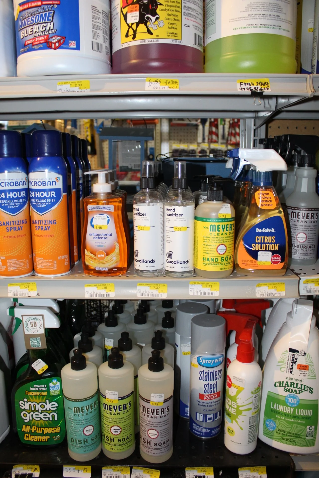 Shelf with cleaning supplies including spray bottles, hand sanitizer, hand soap, dish soap, and laundry liquid in various bottles and containers.