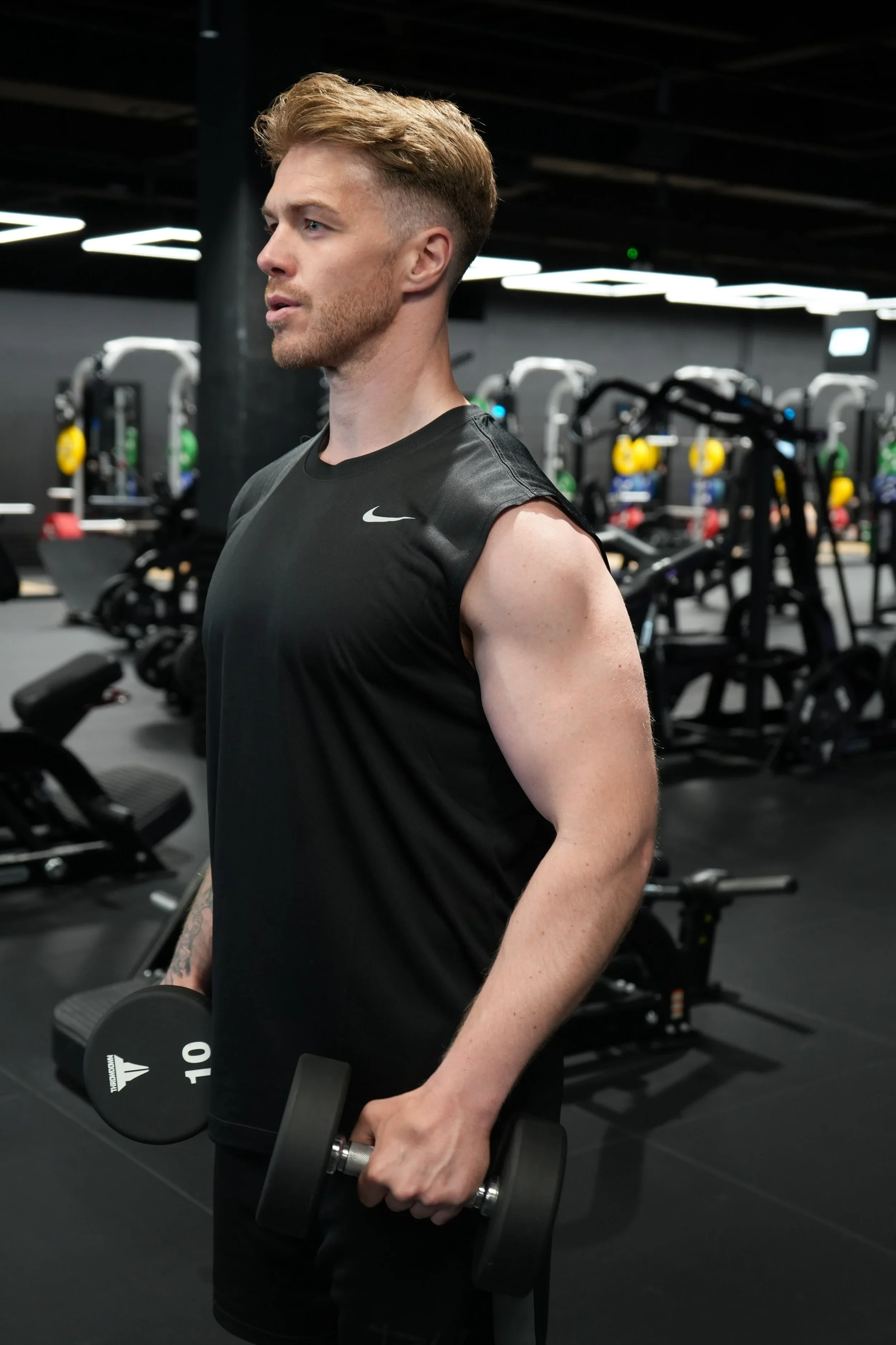 A man in a black athletic shirt lifting a dumbbell in a gym.