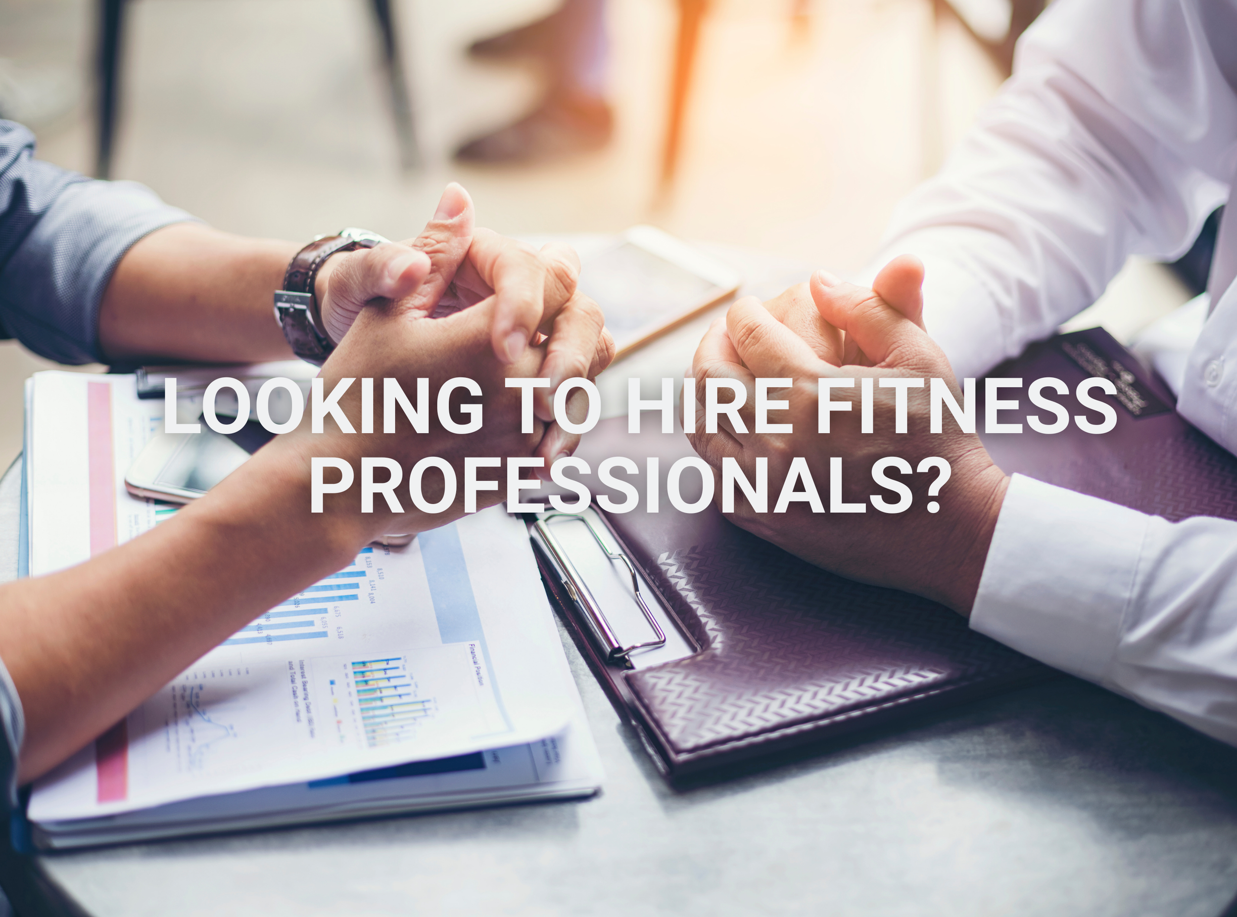 Two people shaking hands in a professional setting with paperwork and a tablet on the table, and the text 'Looking to hire fitness professionals?' overlayed.