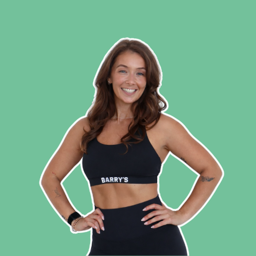 Smiling woman in athletic attire with the word "BARRY'S" on her sports bra, standing with hands on hips against a green background.
